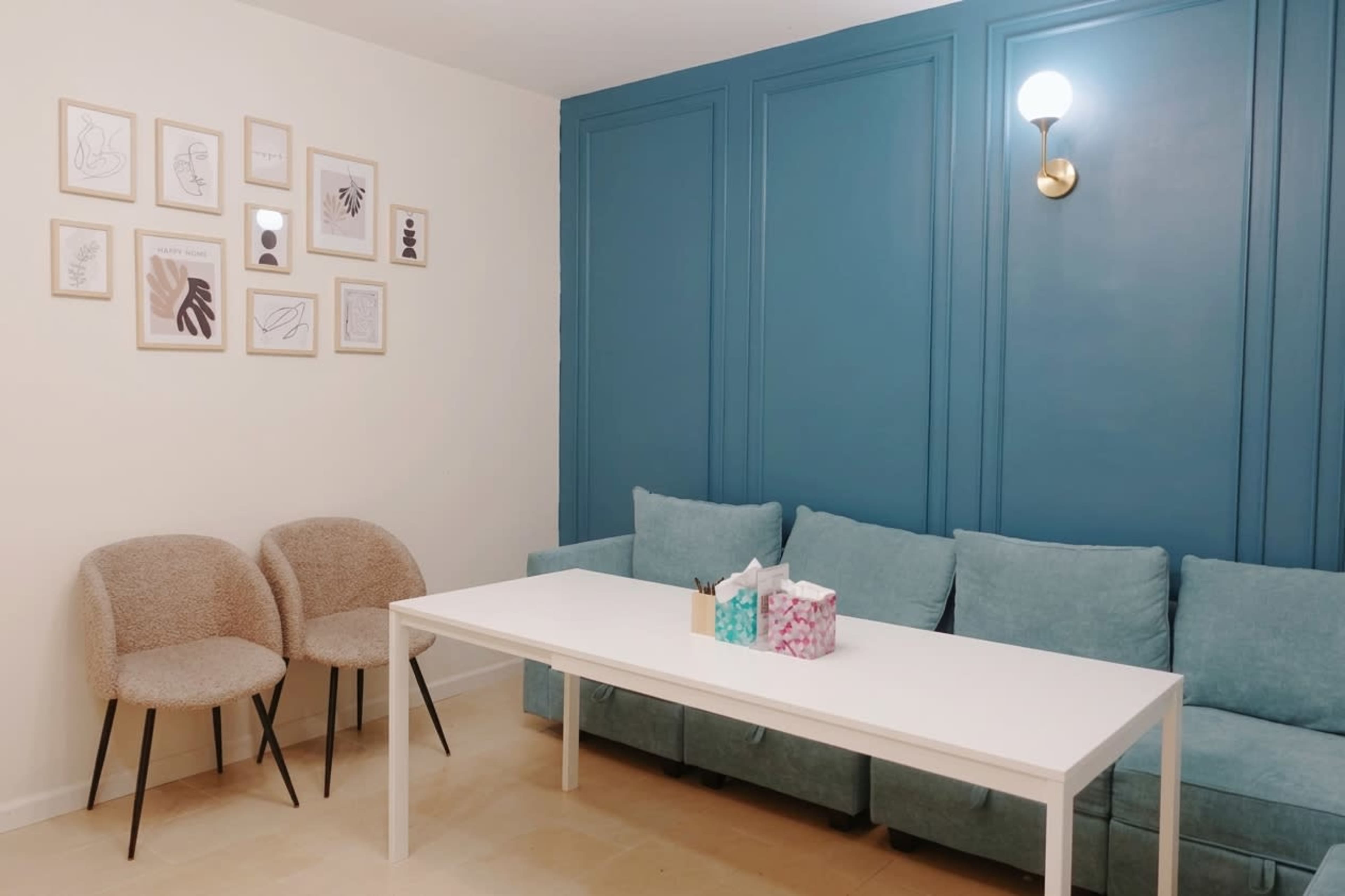 The image shows a living room with a blue accent wall, a white table, a light blue sofa, and two textured chairs, along with framed artwork on the wall.
