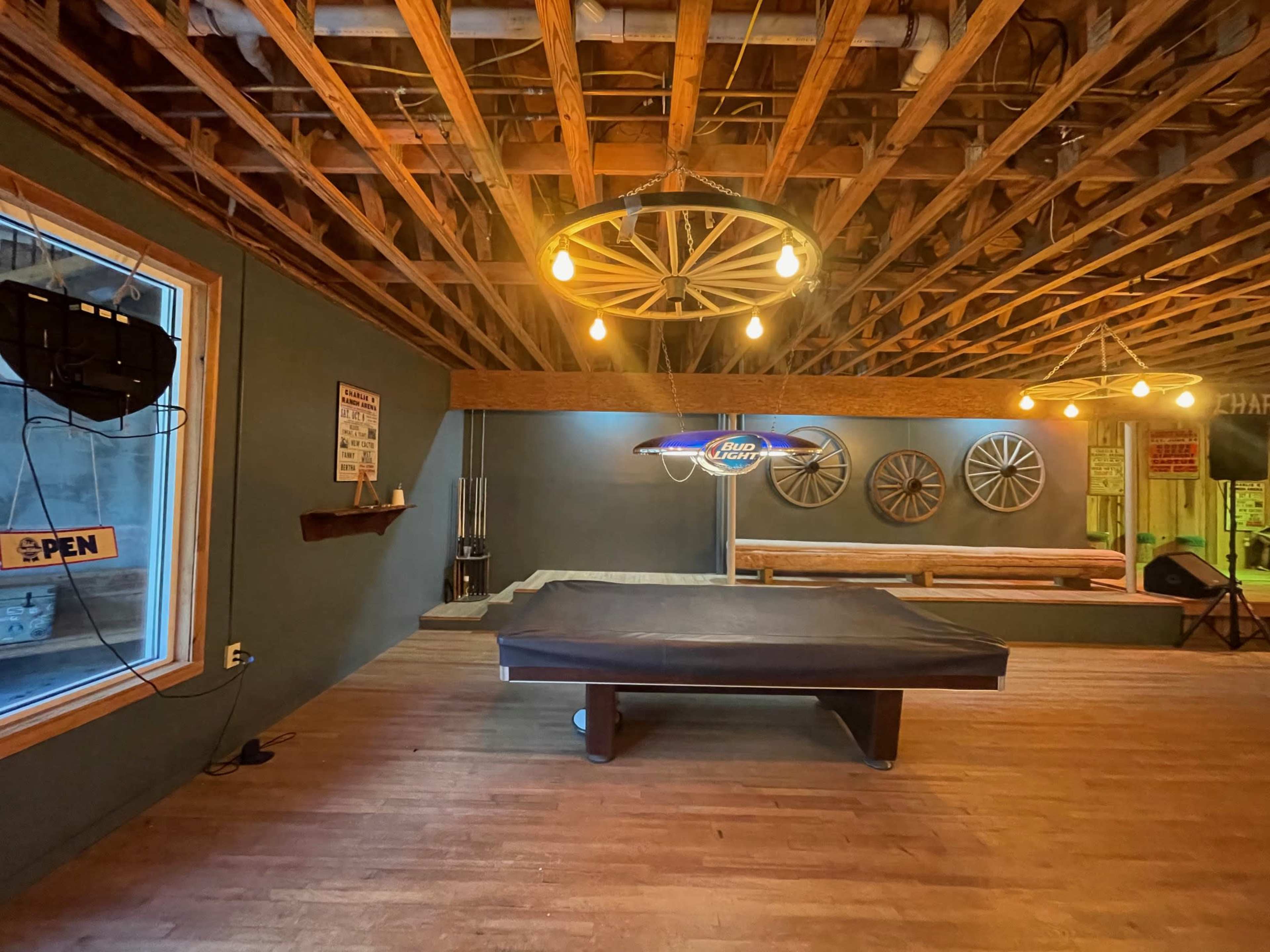 A rustic game room with a pool table, wooden flooring, and exposed beams in the ceiling, along with vintage decor on the walls.