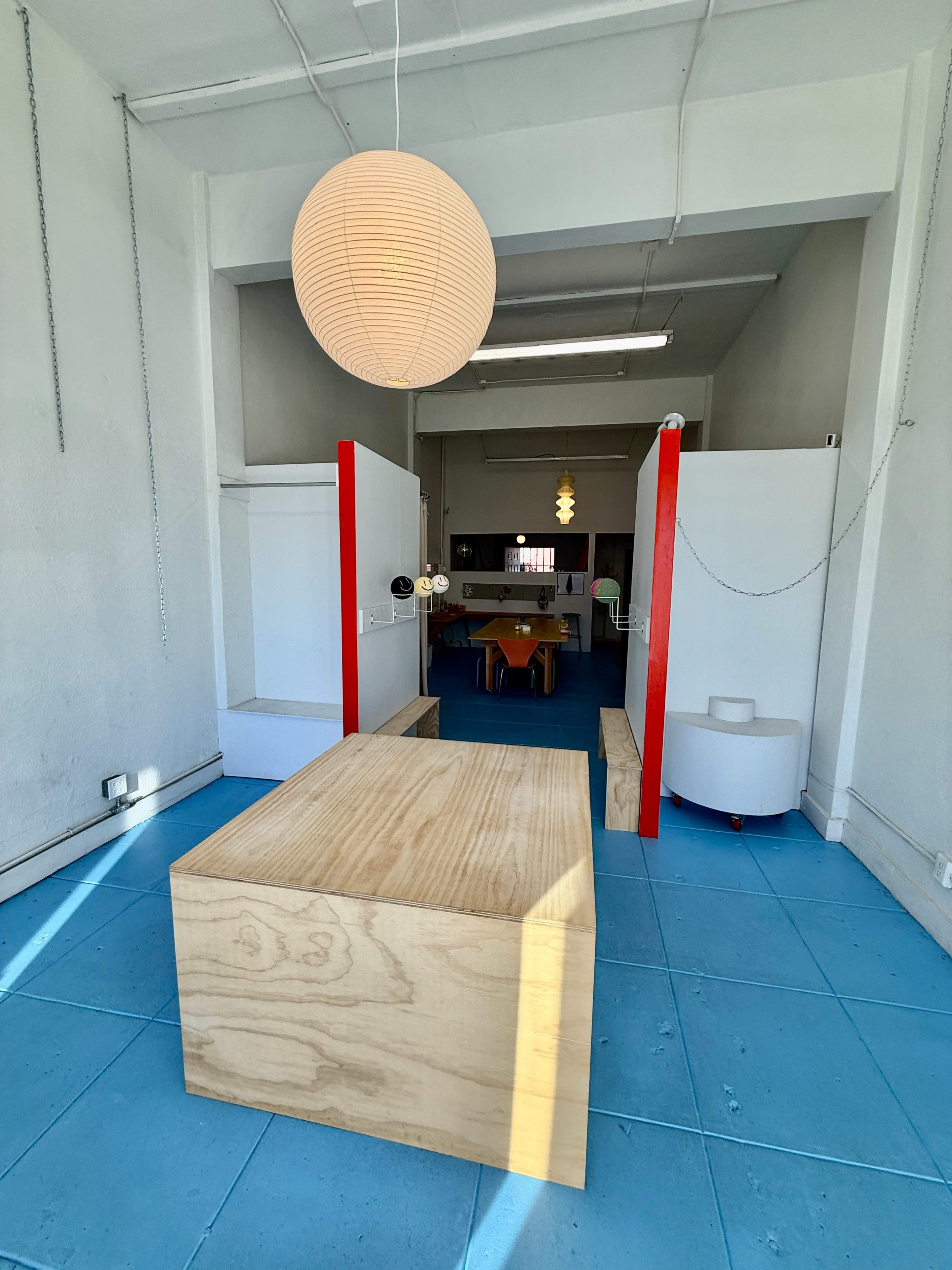 The image shows a spacious interior with blue tiled flooring, featuring wooden furniture, red dividers, and a large hanging light fixture.
