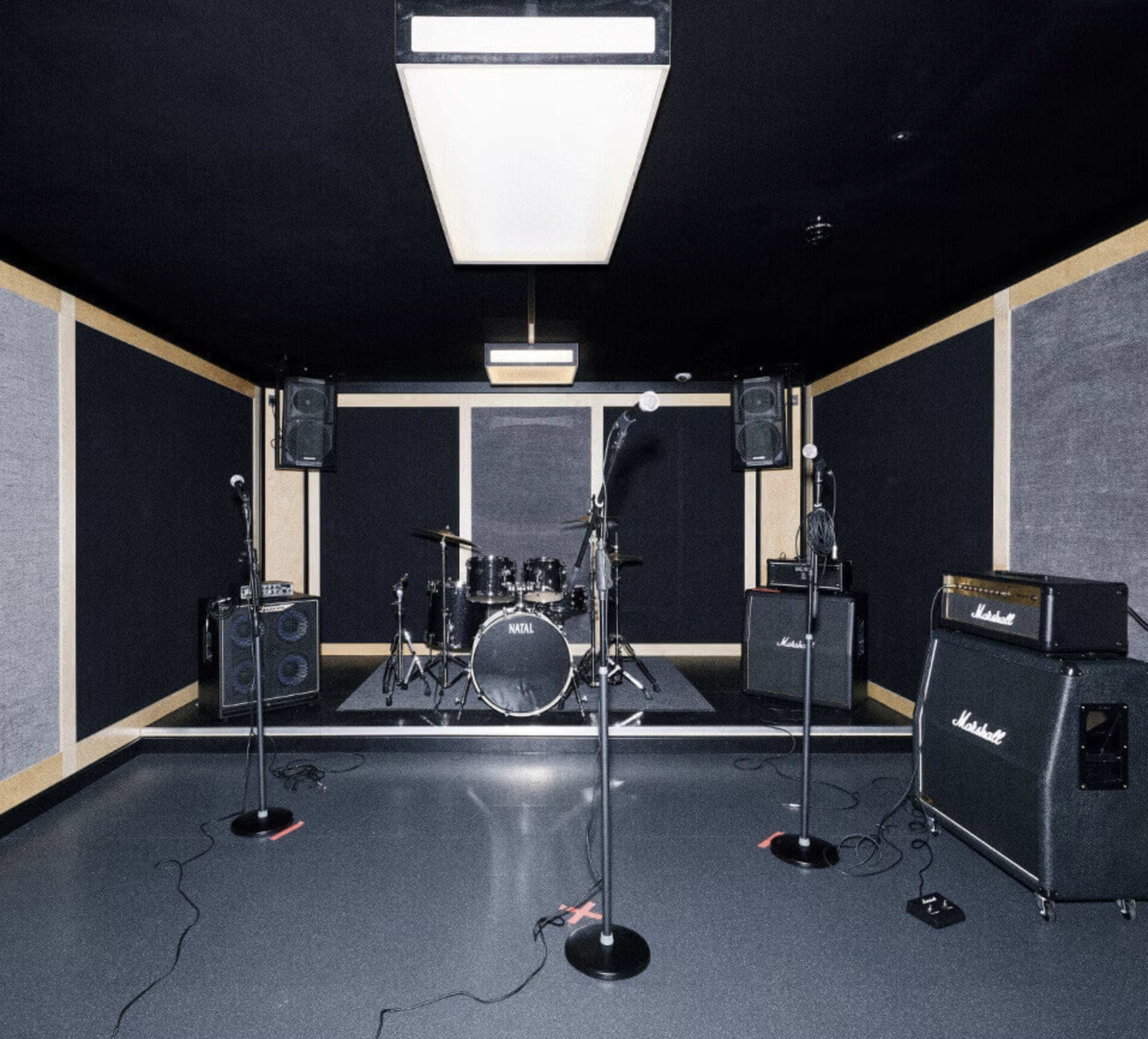 A music rehearsal studio featuring a drum set, amplifiers, and microphones arranged within a soundproofed environment.