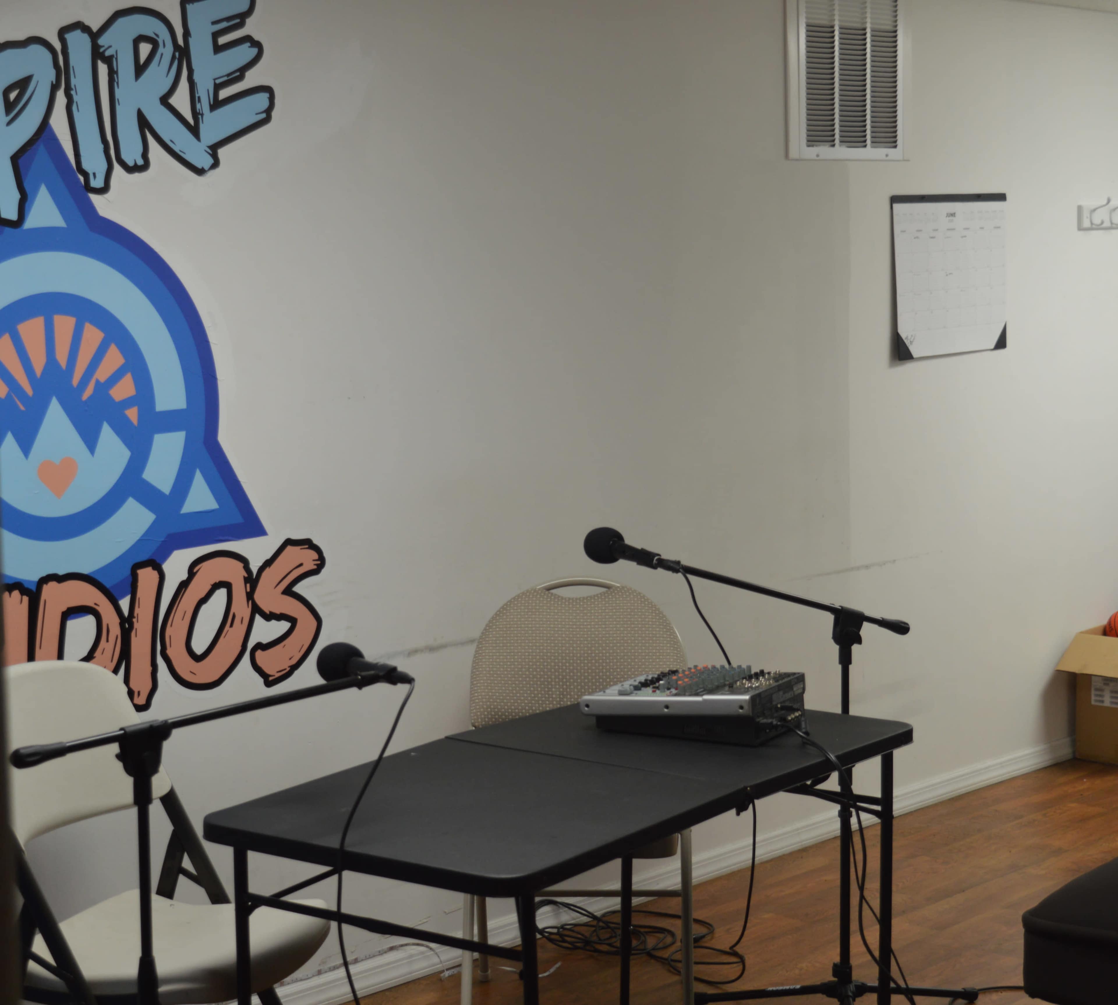 A small recording studio setup with a table, two microphones, and a calendar on the wall.
