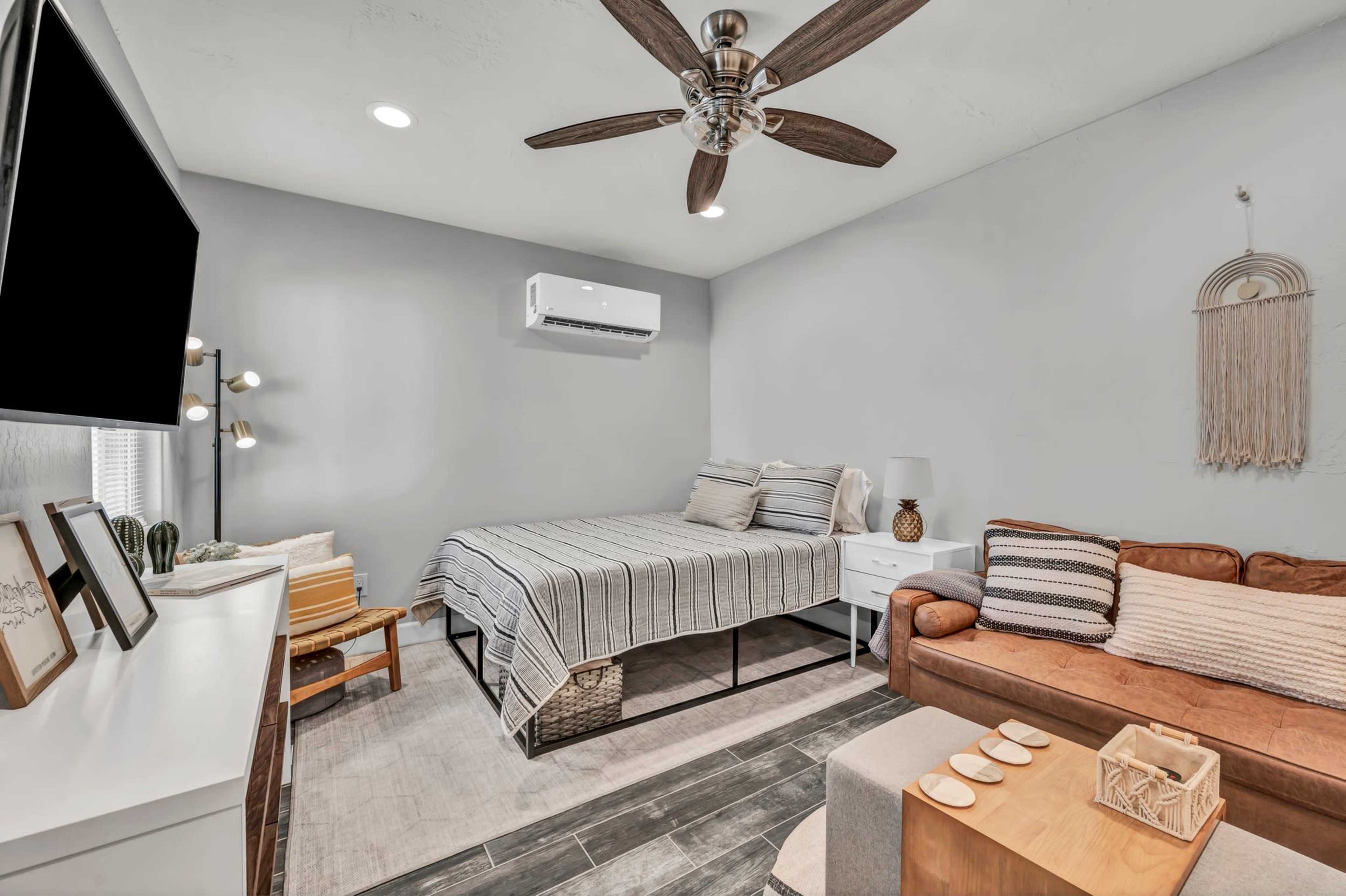 A modern bedroom with a large bed, a brown couch, a wall-mounted television, and a ceiling fan.
