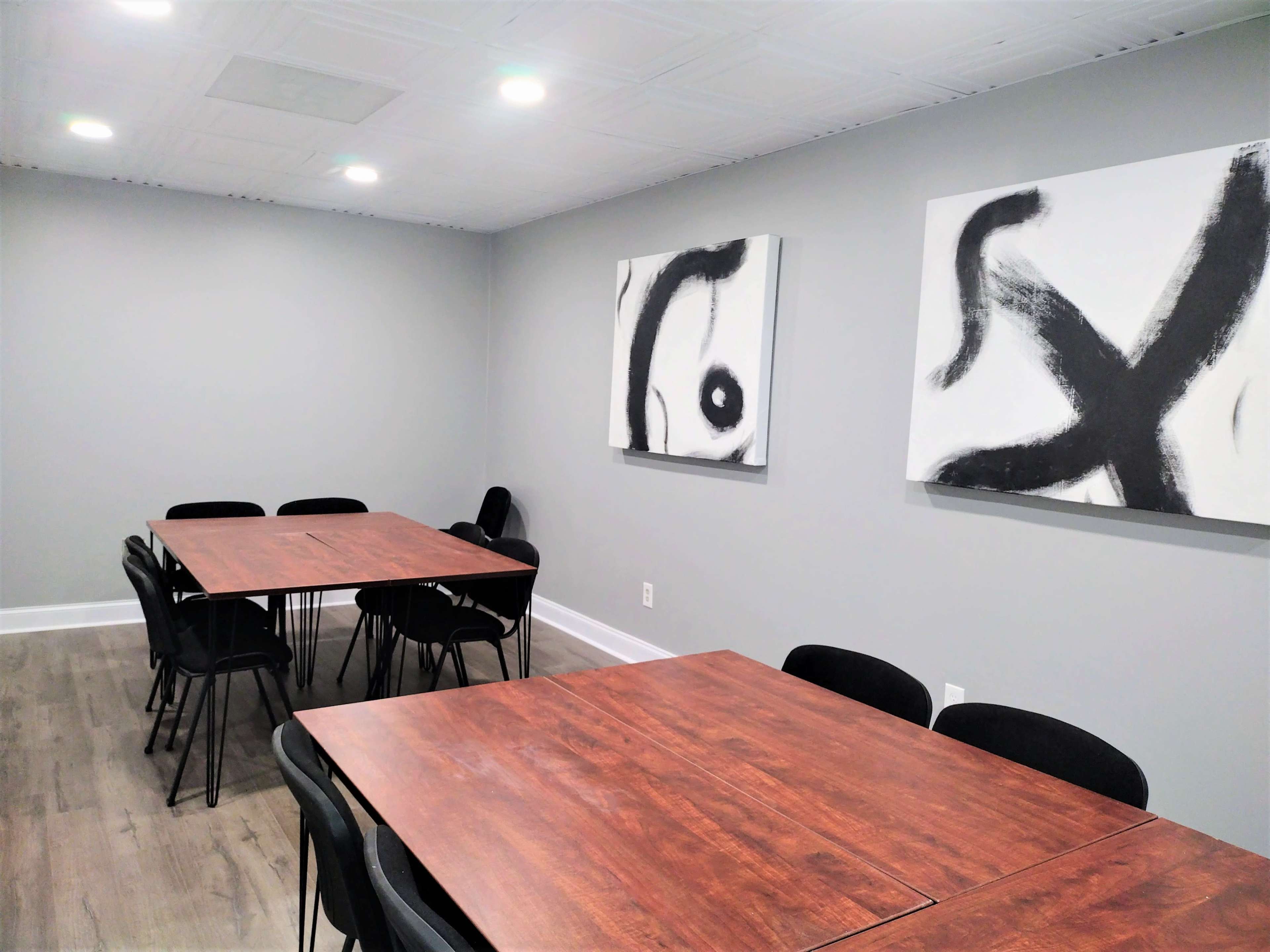 A meeting room with several wooden tables and black chairs, featuring abstract black and white artwork on the walls.