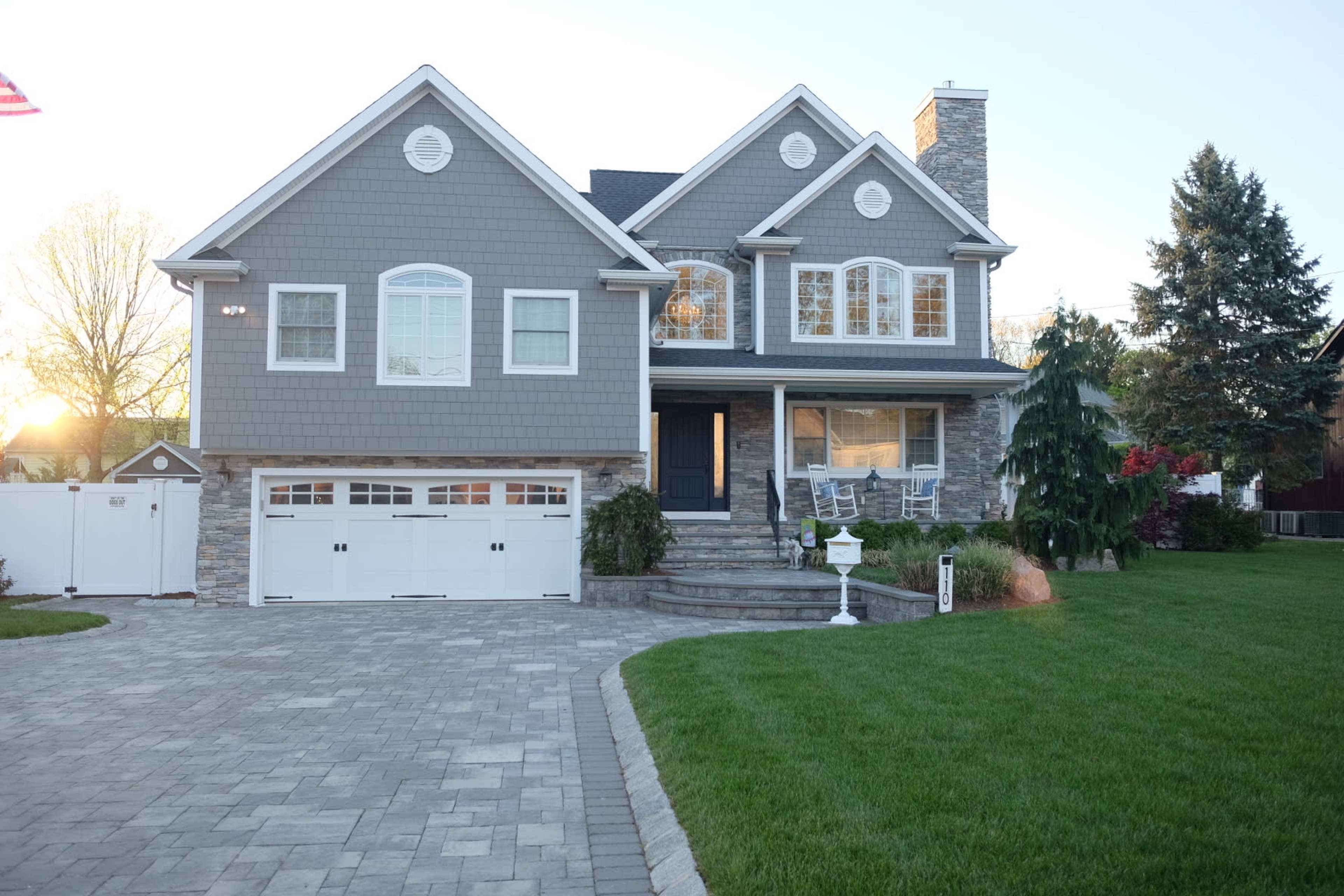 A two-story gray house with a stone facade, a landscaped front yard, and a paved driveway.