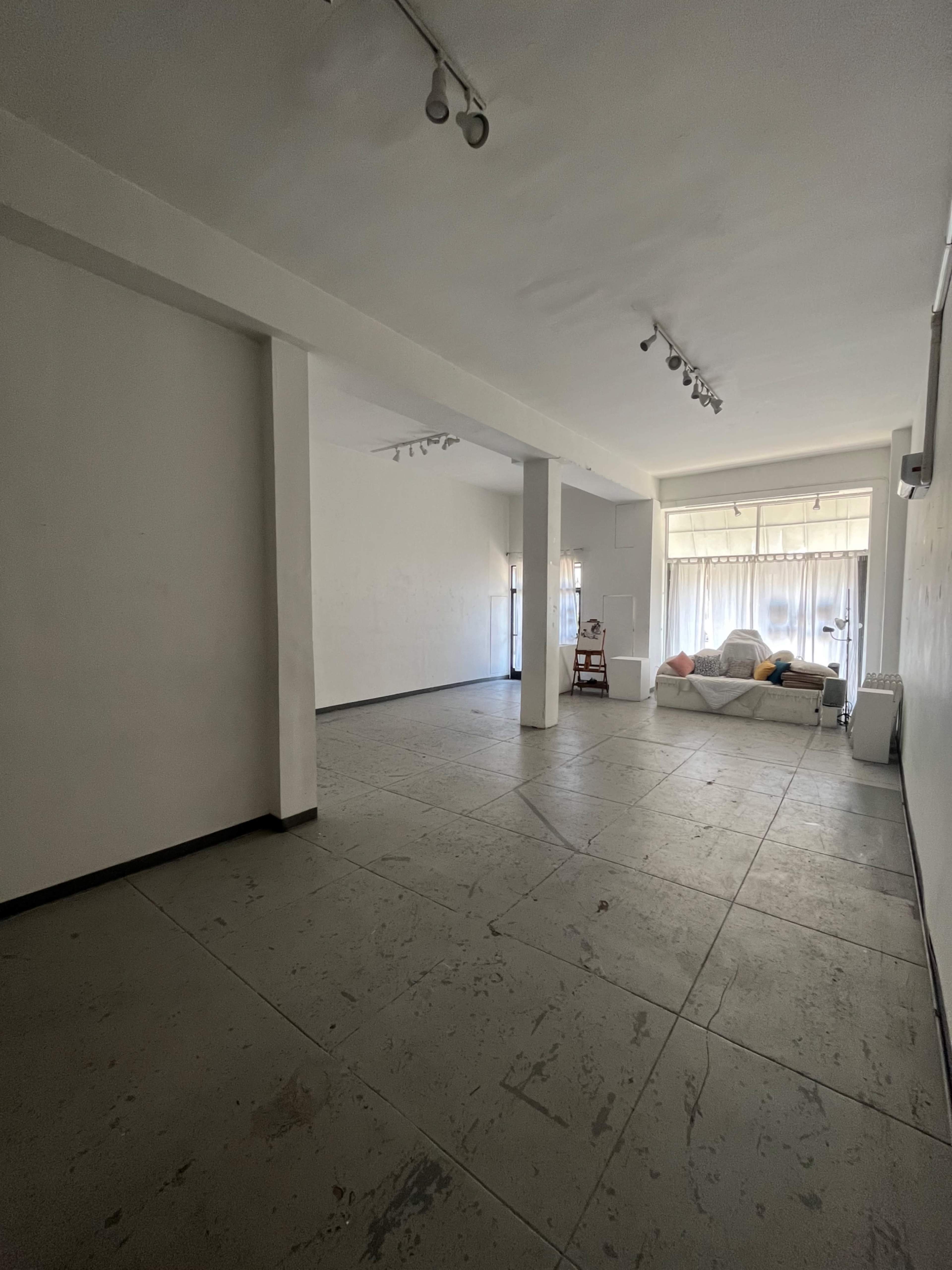 An empty, minimally furnished room with concrete flooring and large windows at one end.