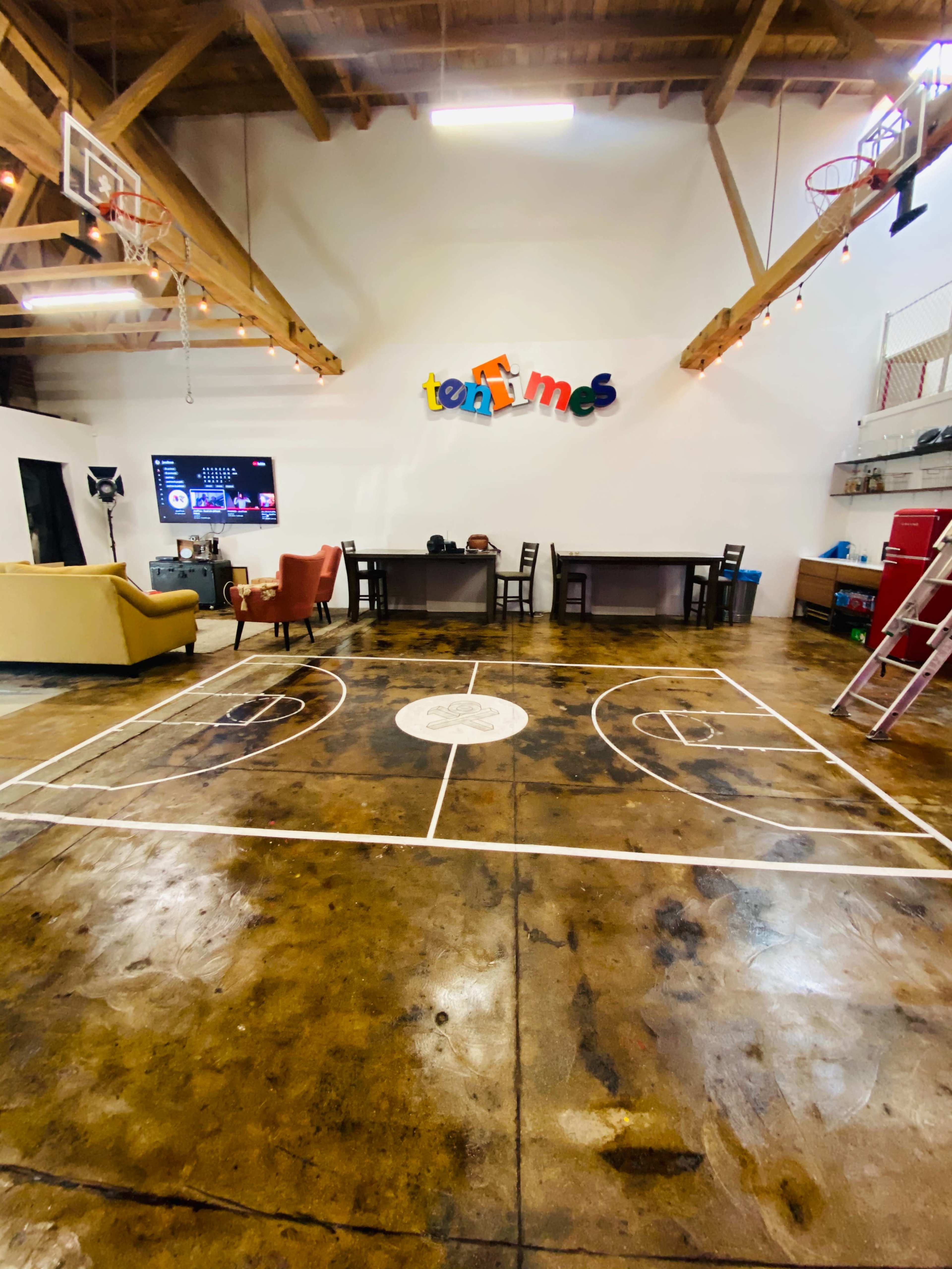 A spacious room with a basketball court floor design, surrounded by chairs, tables, and a television mounted on the wall.