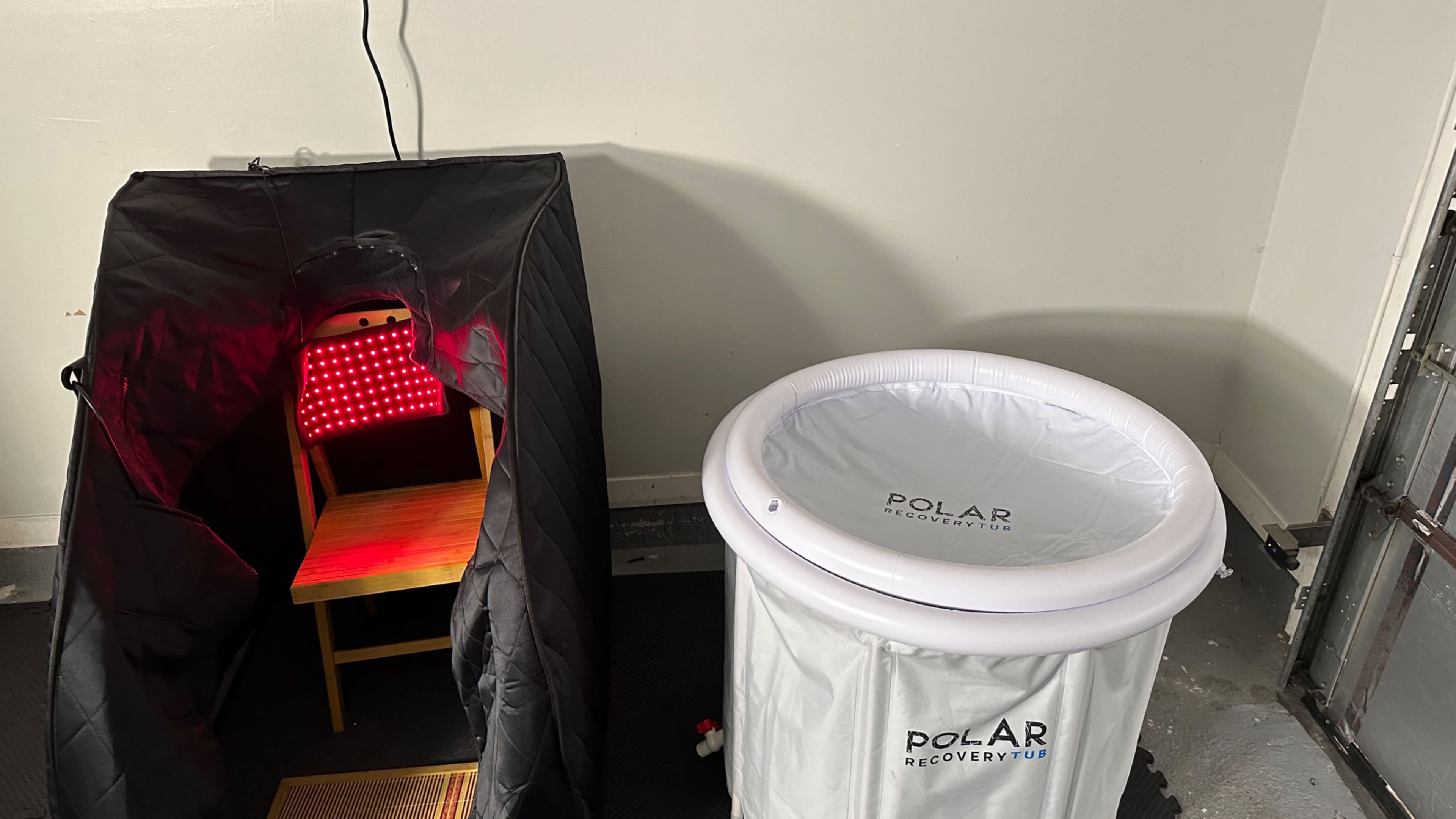 A black sauna-like tent with a chair inside next to a white recovery tub labeled "POLAR RECOVERY."