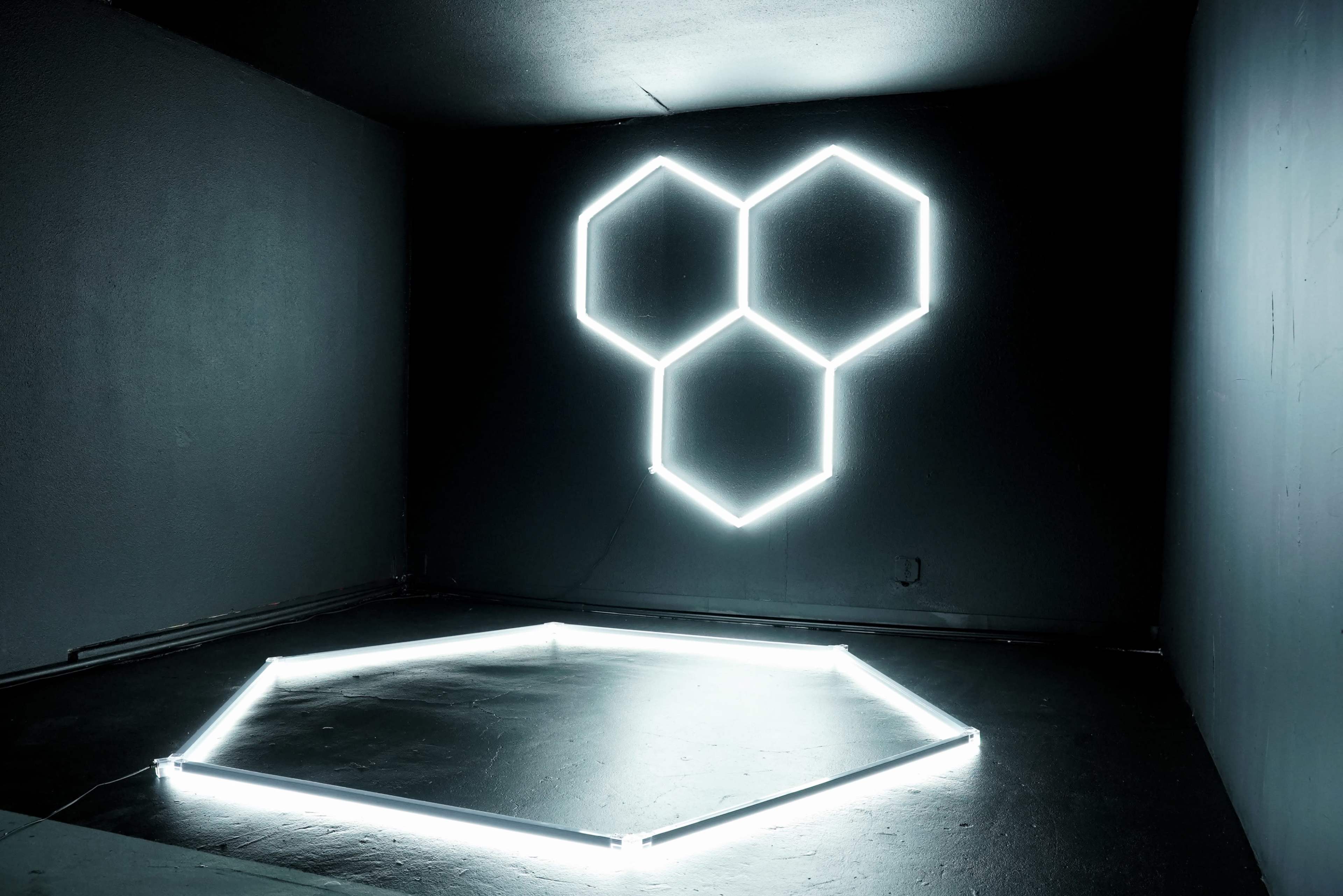 The image shows a dark room with glowing hexagonal neon lights arranged on the wall and floor.