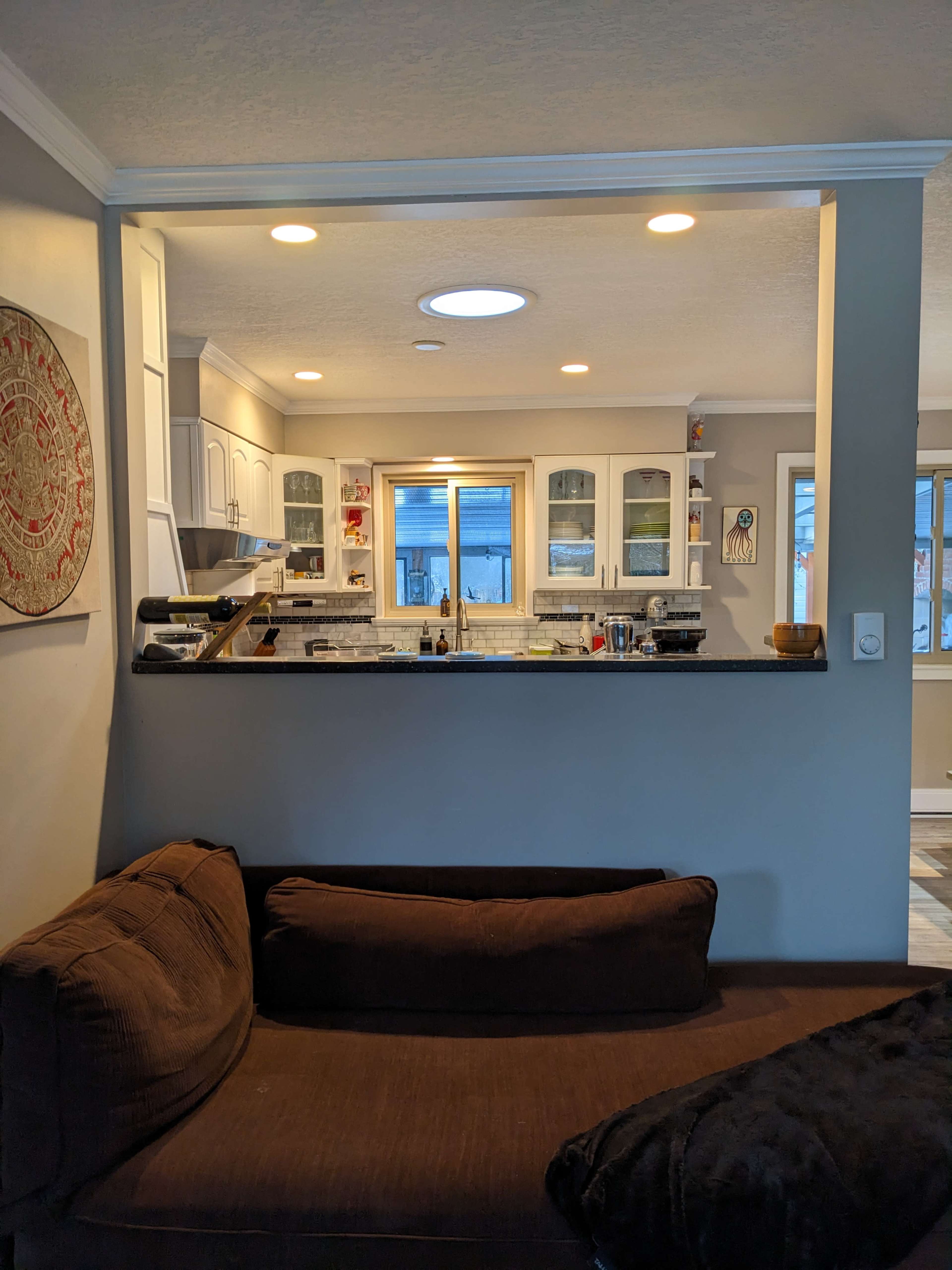 A cozy living space with a brown couch facing an open kitchen that features white cabinets and a countertop.