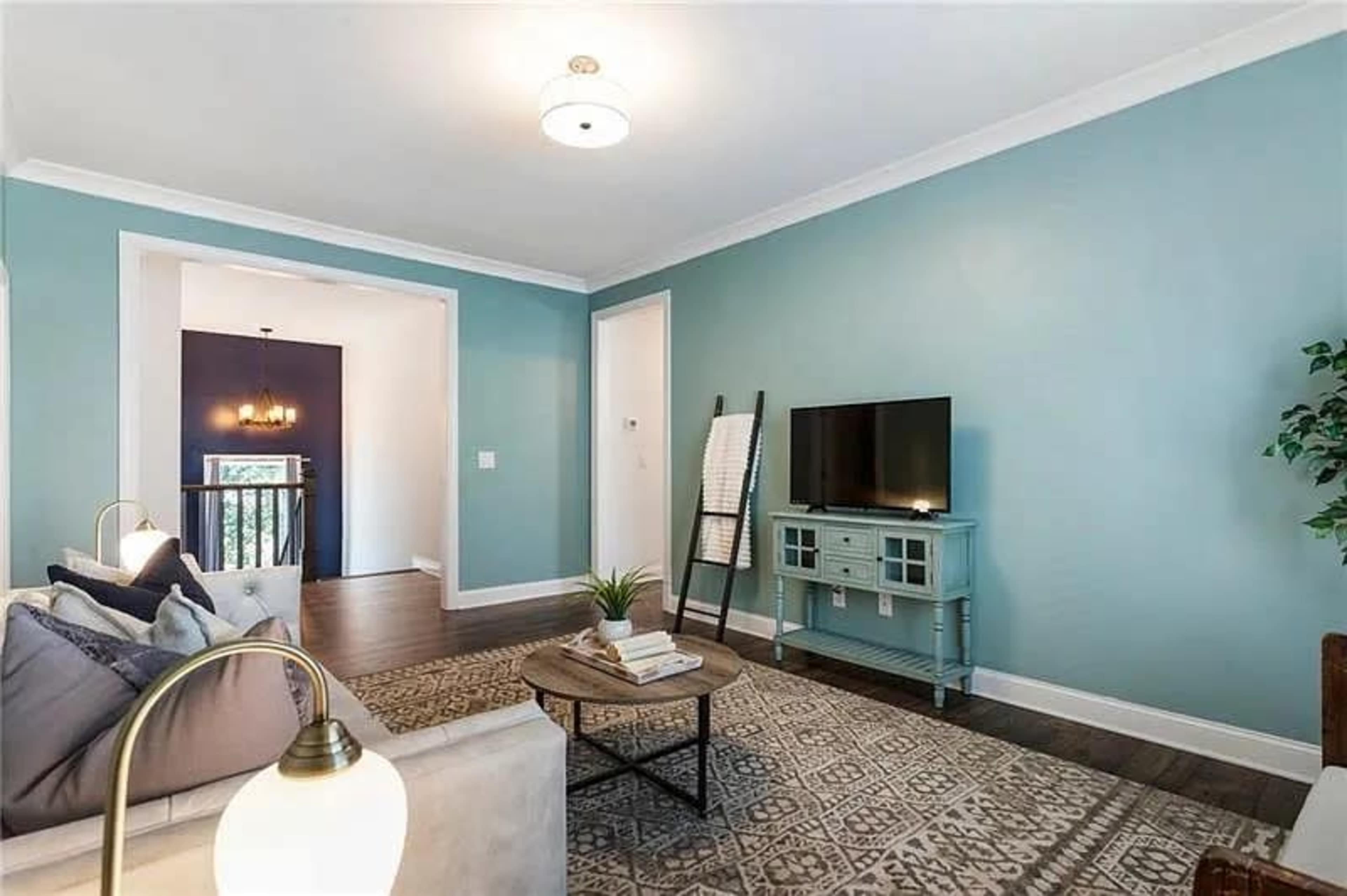 The image shows a living room with light teal walls, a television on a stand, a decorative coffee table, and a couch with cushions.