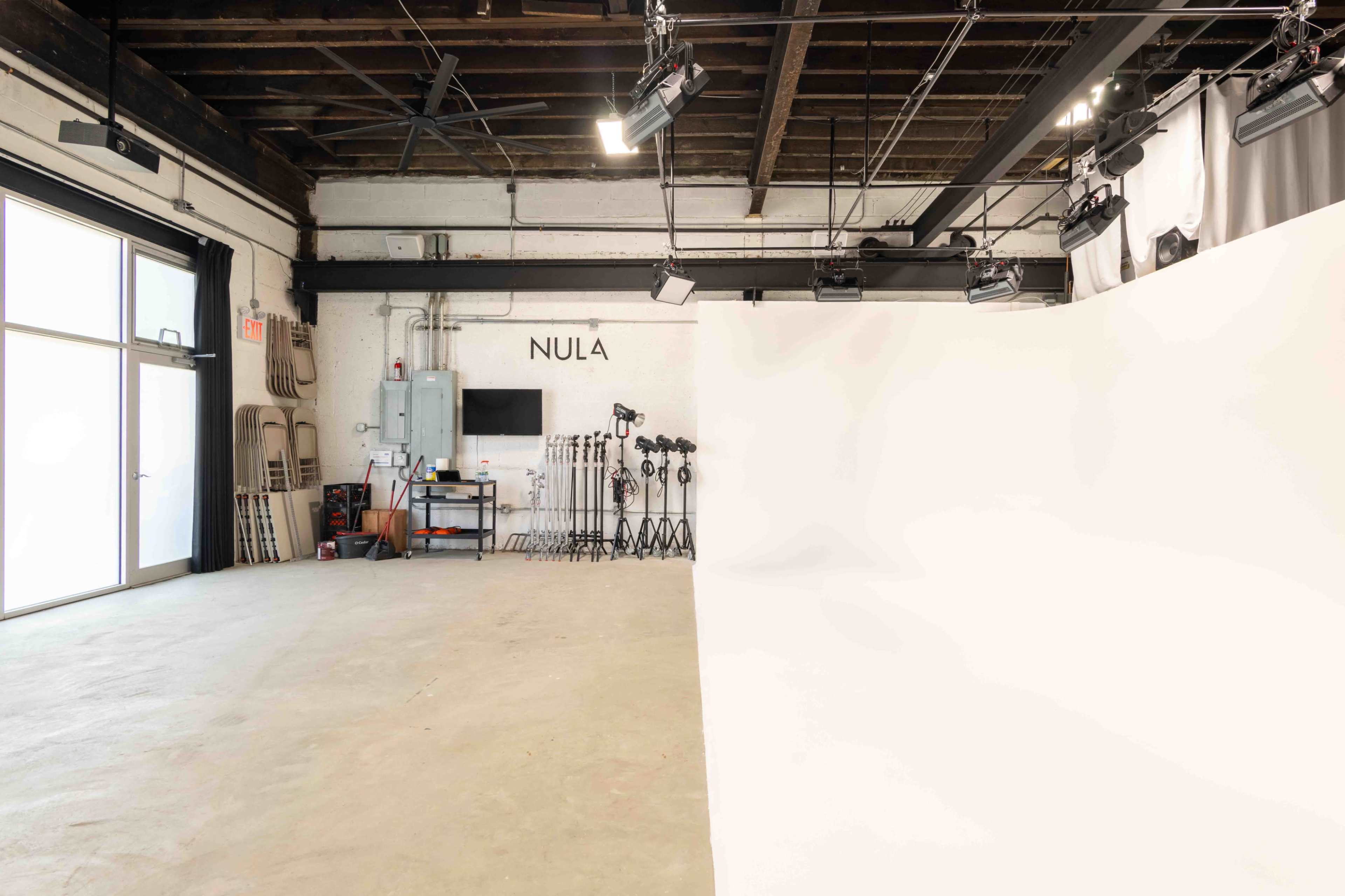 The image shows an empty photo studio with white backdrop, lighting equipment, and a clean concrete floor.