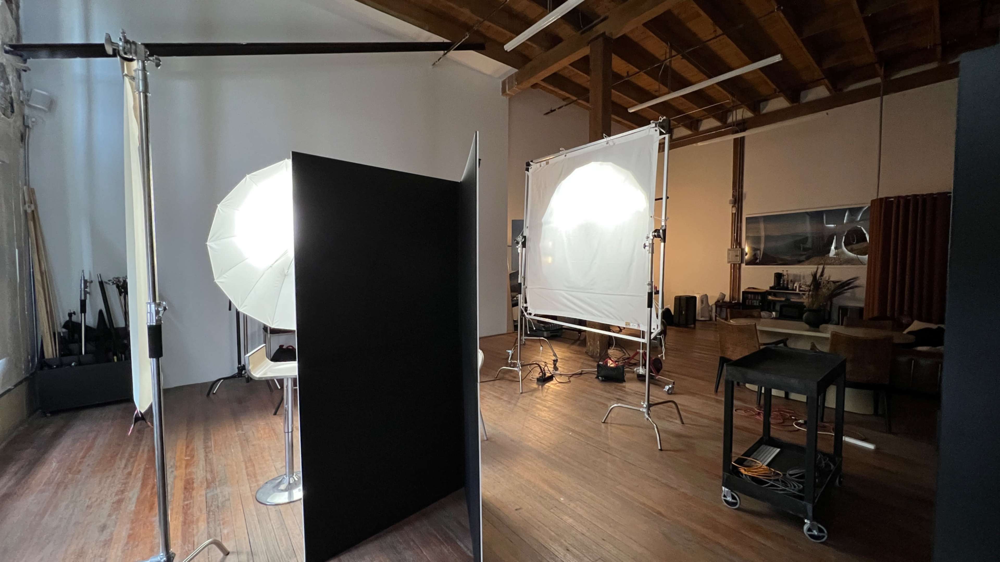The image shows a photography studio with softbox lights, light reflectors, and various backdrops set up in a spacious wooden-floored area.