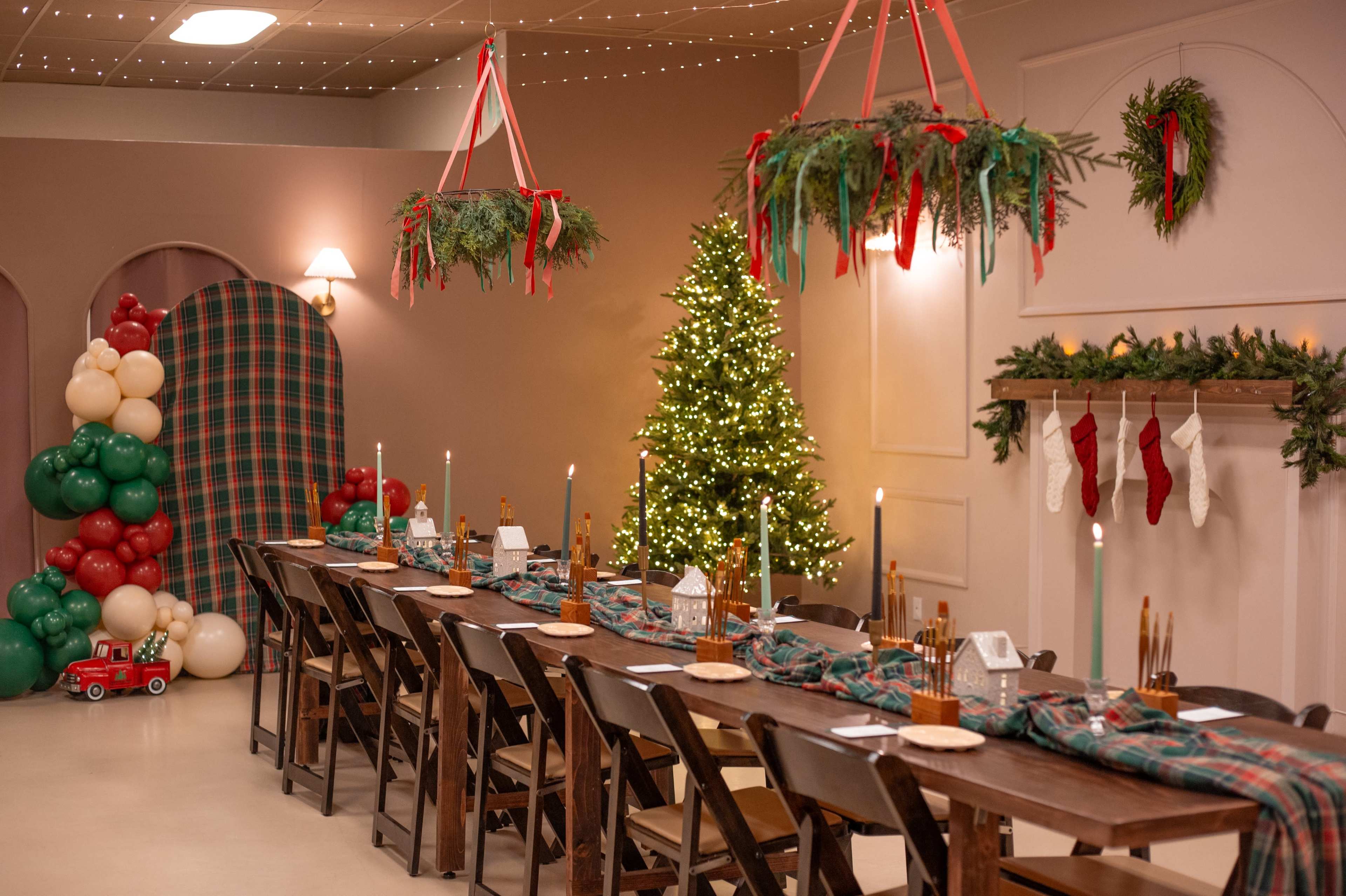 A decorated dining area features a long wooden table with candles, festive table settings, a Christmas tree, and holiday accents on the walls and ceiling.