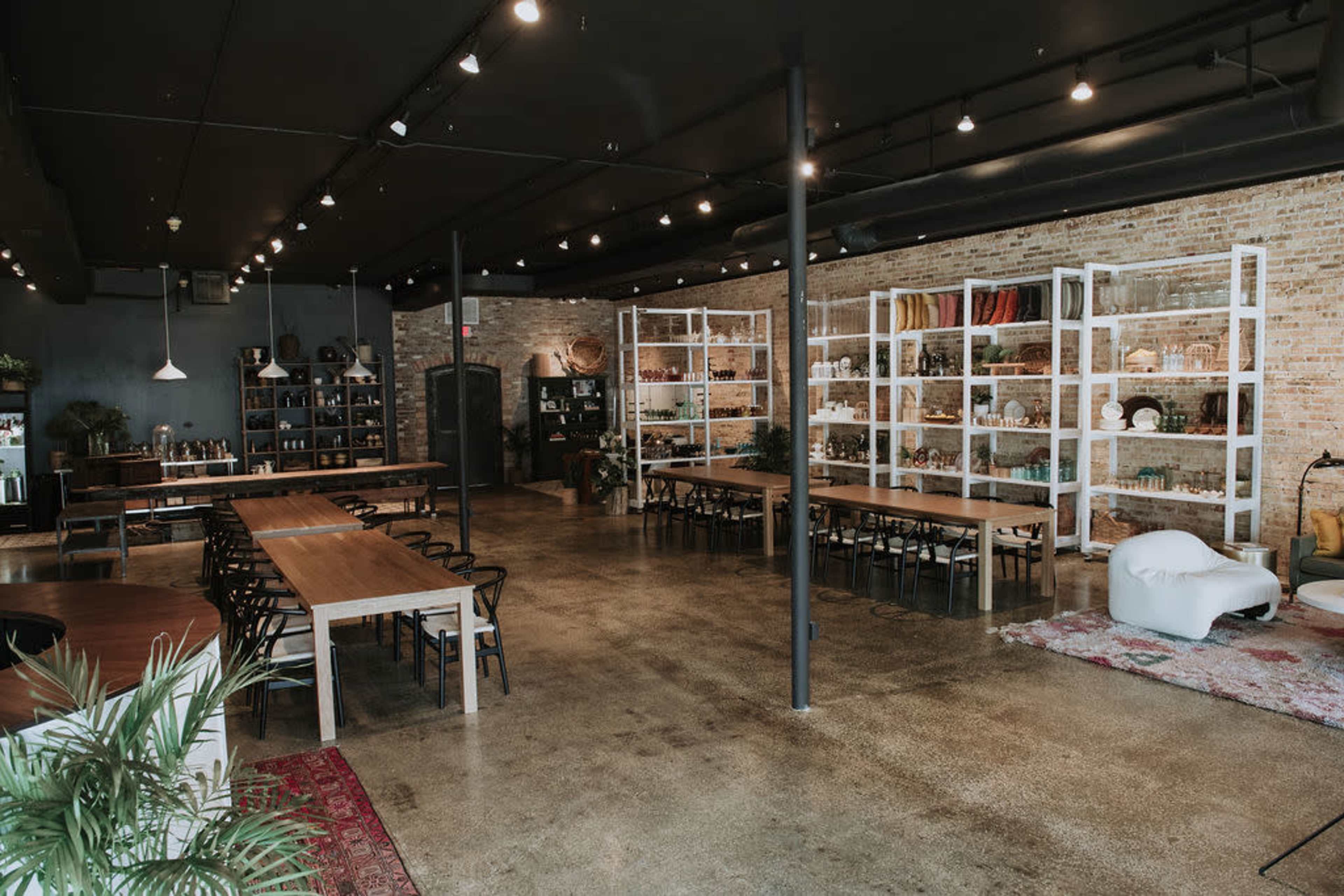 A spacious, industrial-style room with wooden tables, black chairs, and shelves filled with various decorative items.