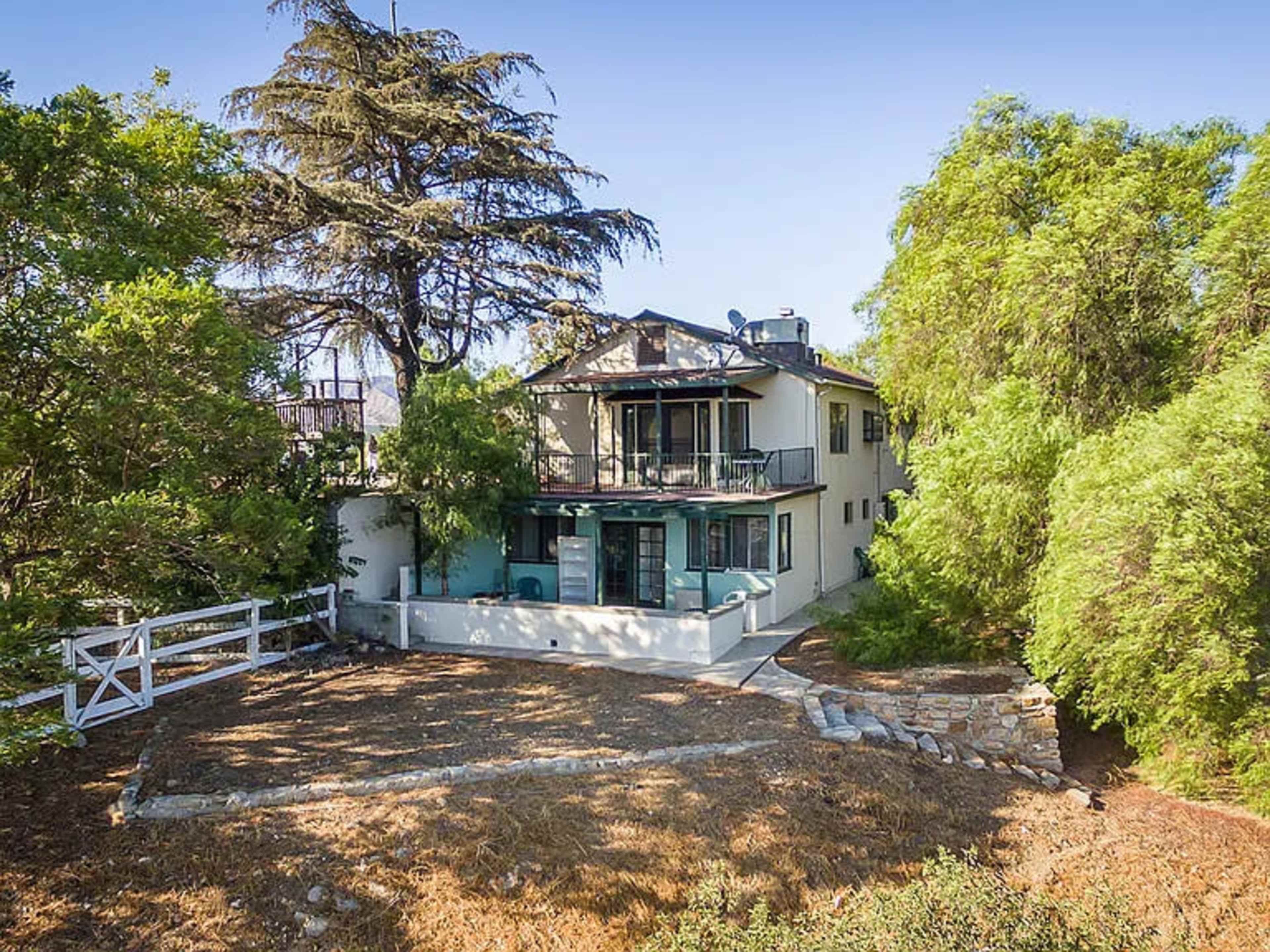 A two-story house surrounded by trees, with a patio and a stone pathway leading to it.