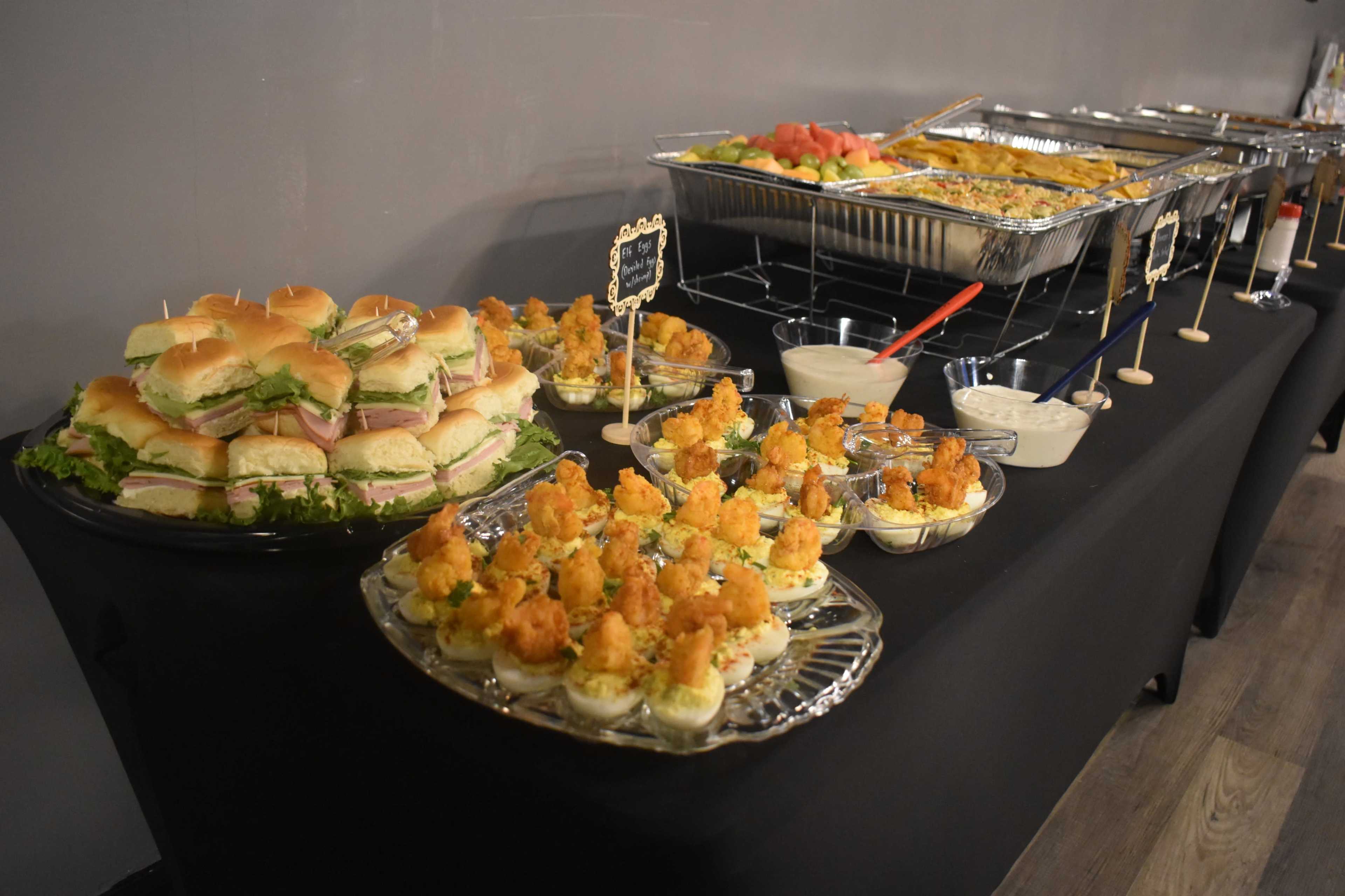 A buffet table featuring trays of sandwiches, shrimp cocktails, and assorted appetizers.