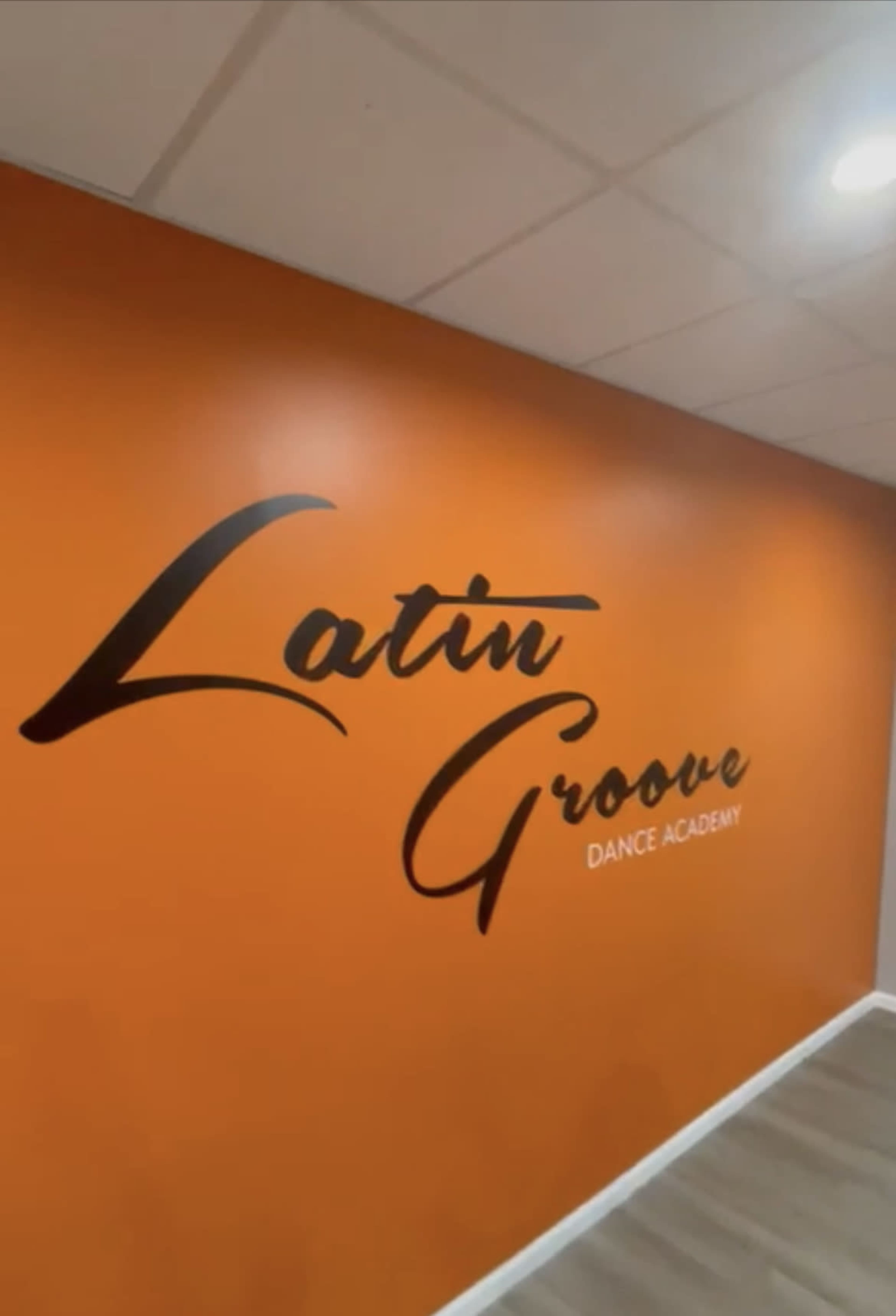 The image shows an orange wall featuring the text "Latin Groove Dance Academy" in a stylish font.