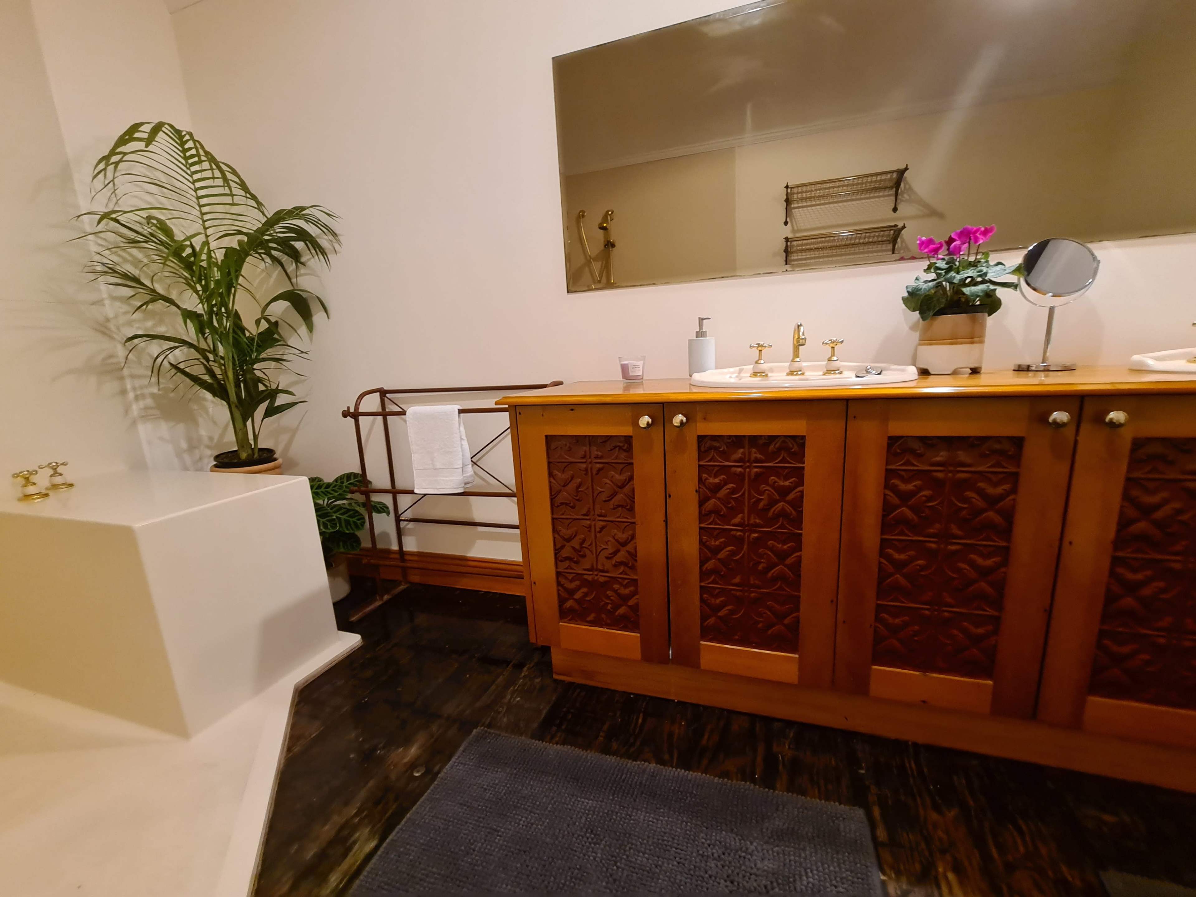 The image shows a bathroom with a wooden vanity featuring decorative cabinet doors, a large mirror, a potted plant, and a freestanding tub.