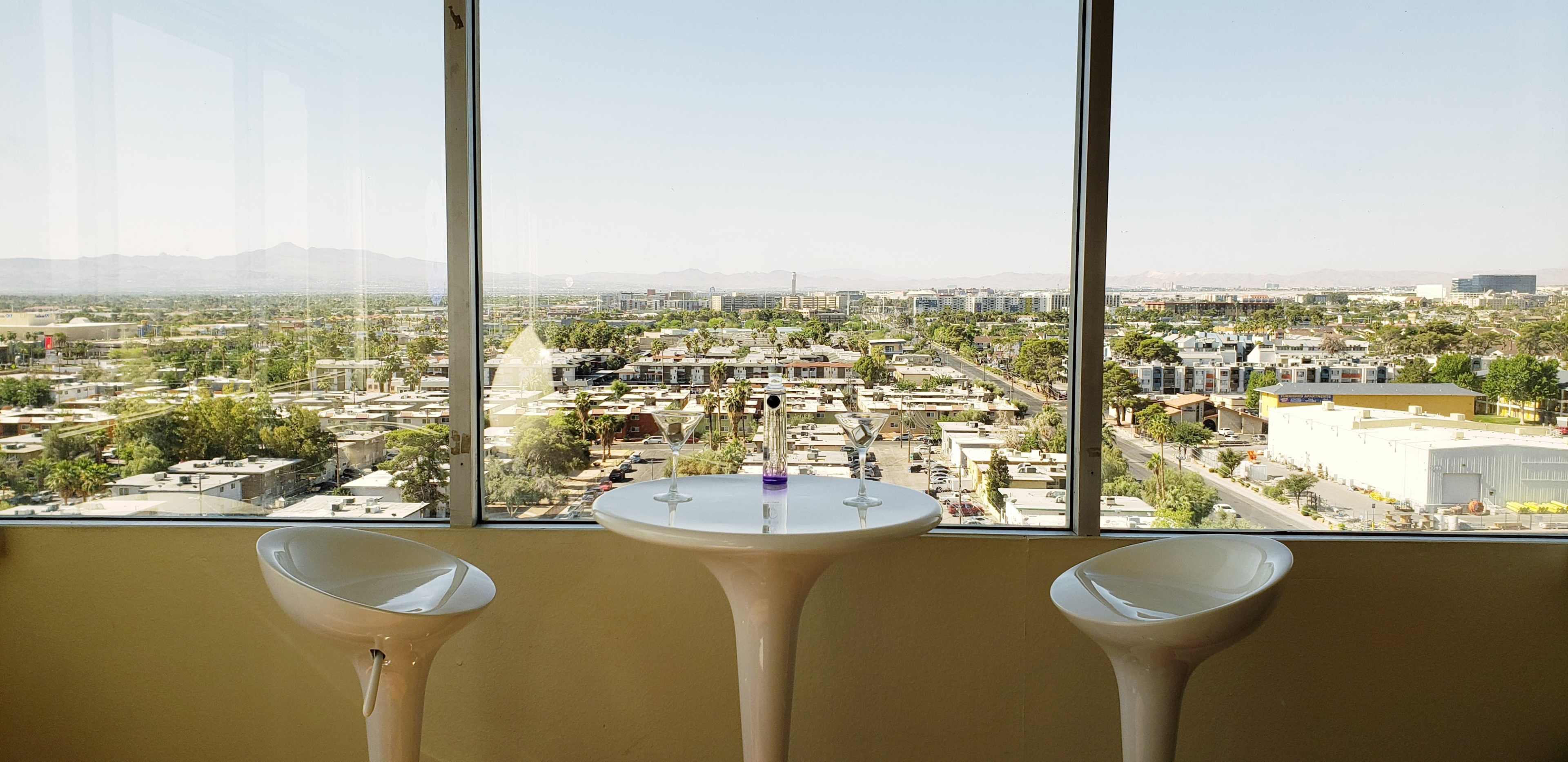 A bright room with two white chairs and a small round table, overlooking a sprawling urban landscape through large windows.