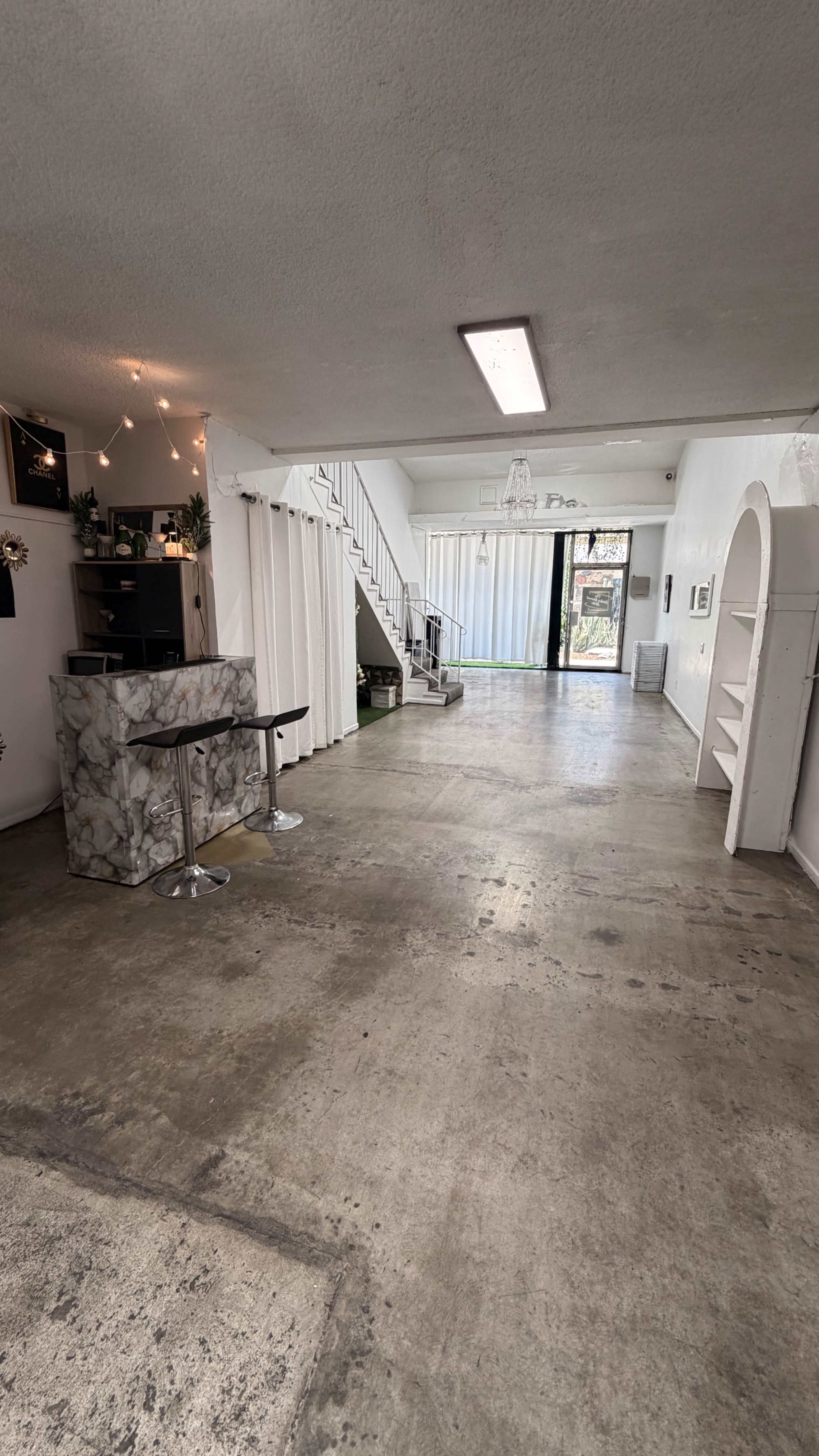 The image shows a spacious interior area with a marble-topped bar, a staircase leading to an upper level, and large windows providing natural light.