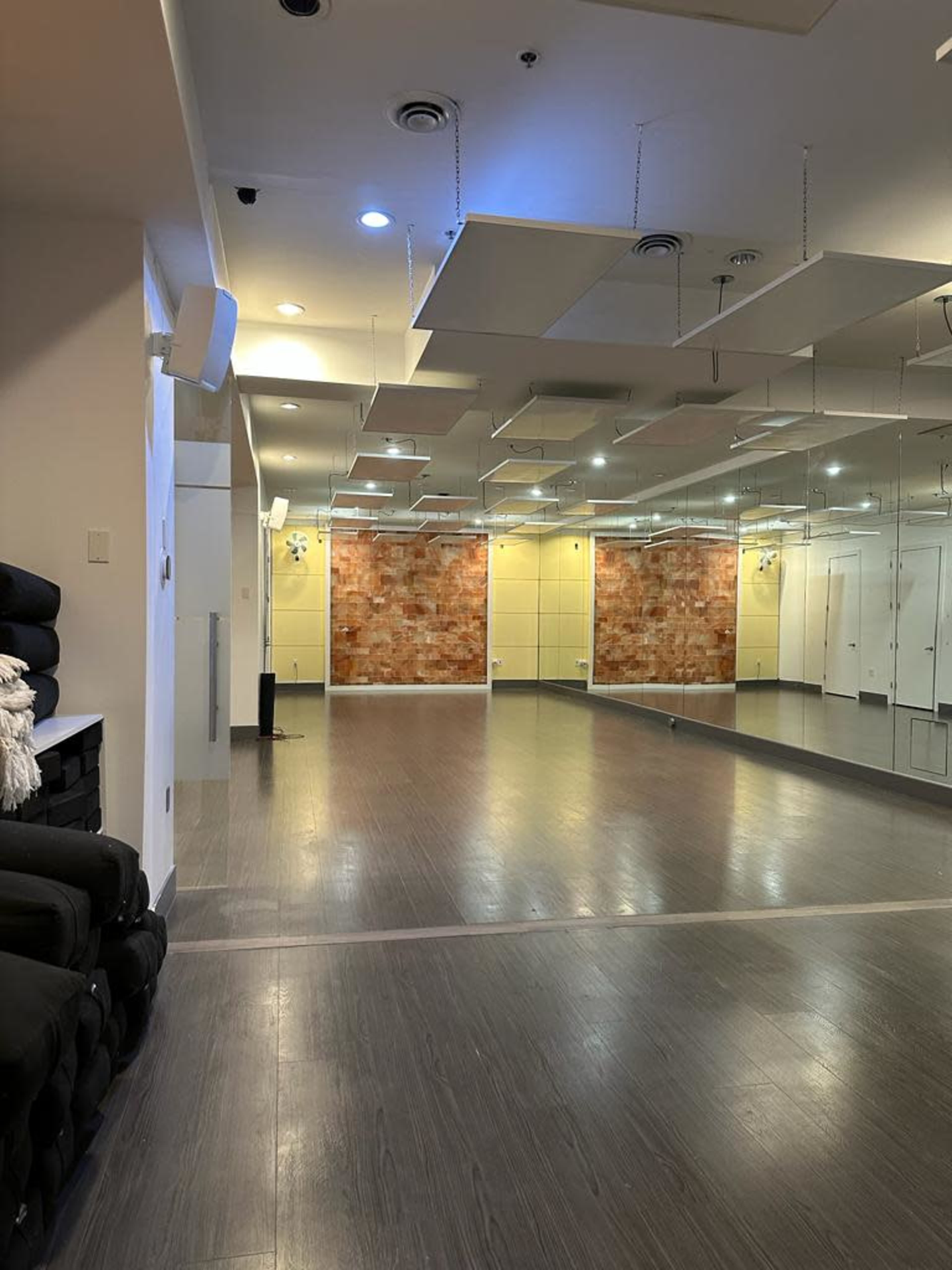 An empty fitness studio with mirrored walls, wooden flooring, and a textured feature wall.