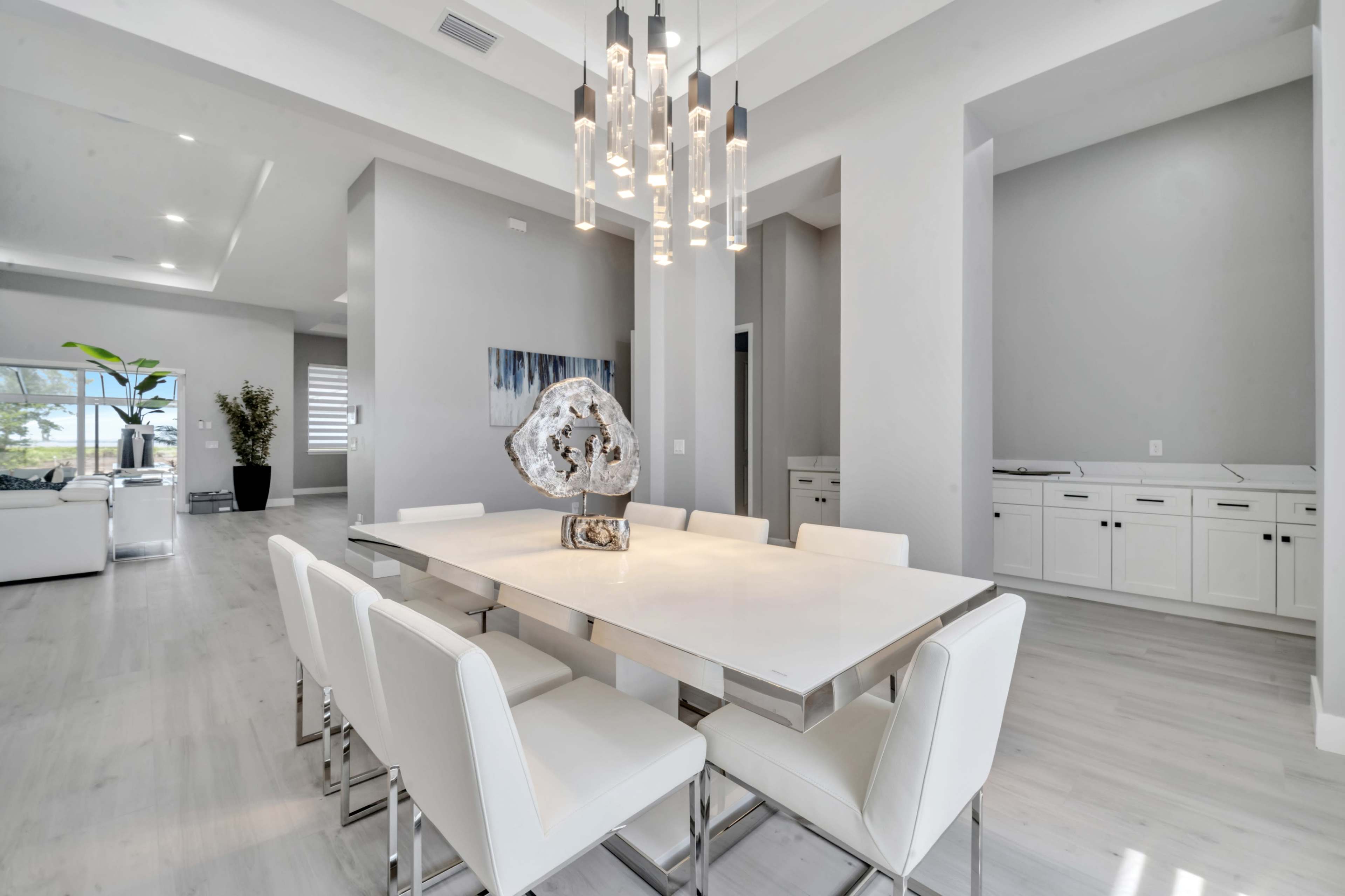 A modern dining area features a sleek table surrounded by white chairs, with a statement light fixture overhead and minimalistic decor.