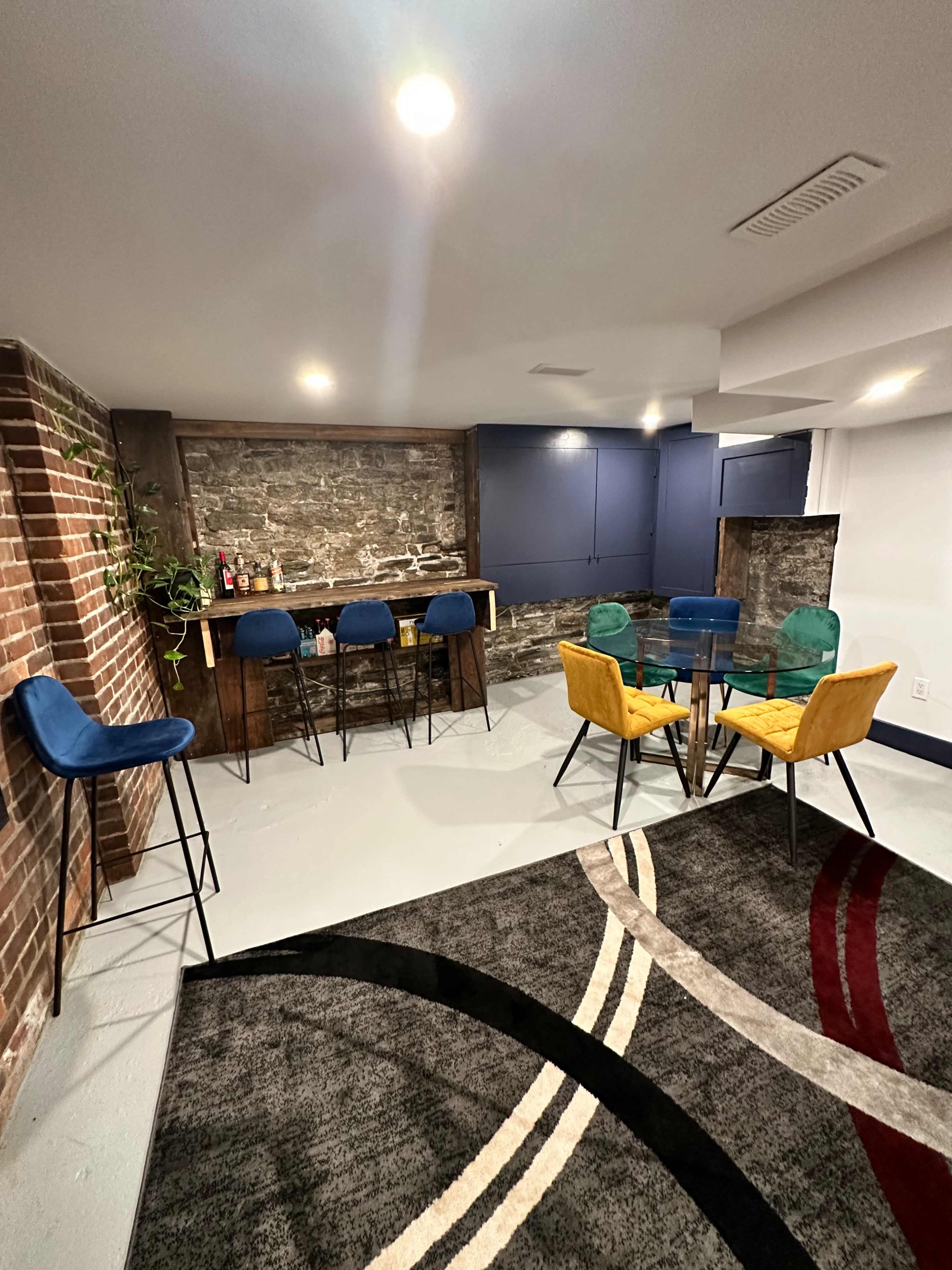 A modern basement bar area with a seating arrangement that includes colorful chairs and a stone wall backdrop.
