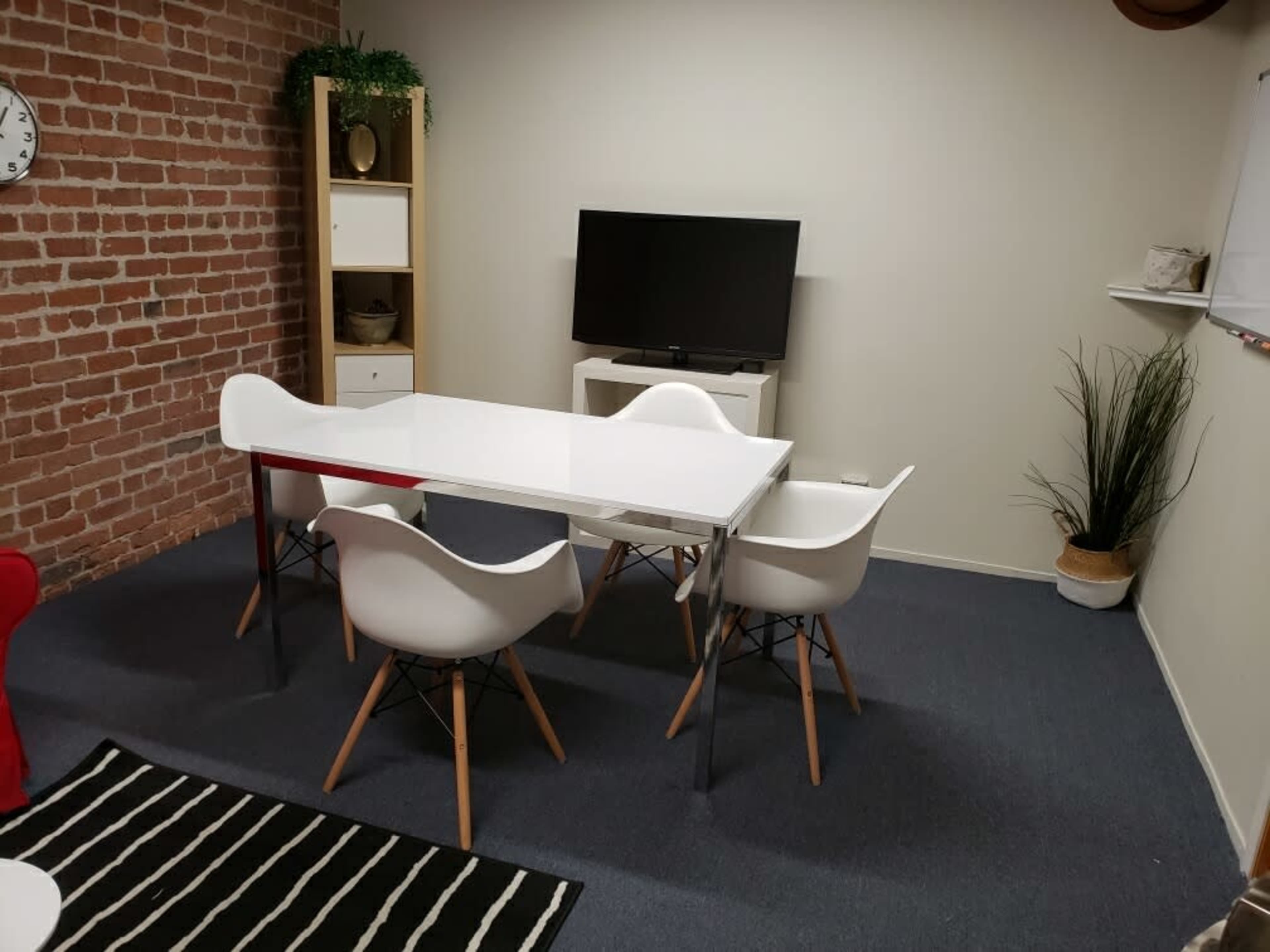 A small meeting room featuring a white table surrounded by four chairs and a television mounted on the wall.