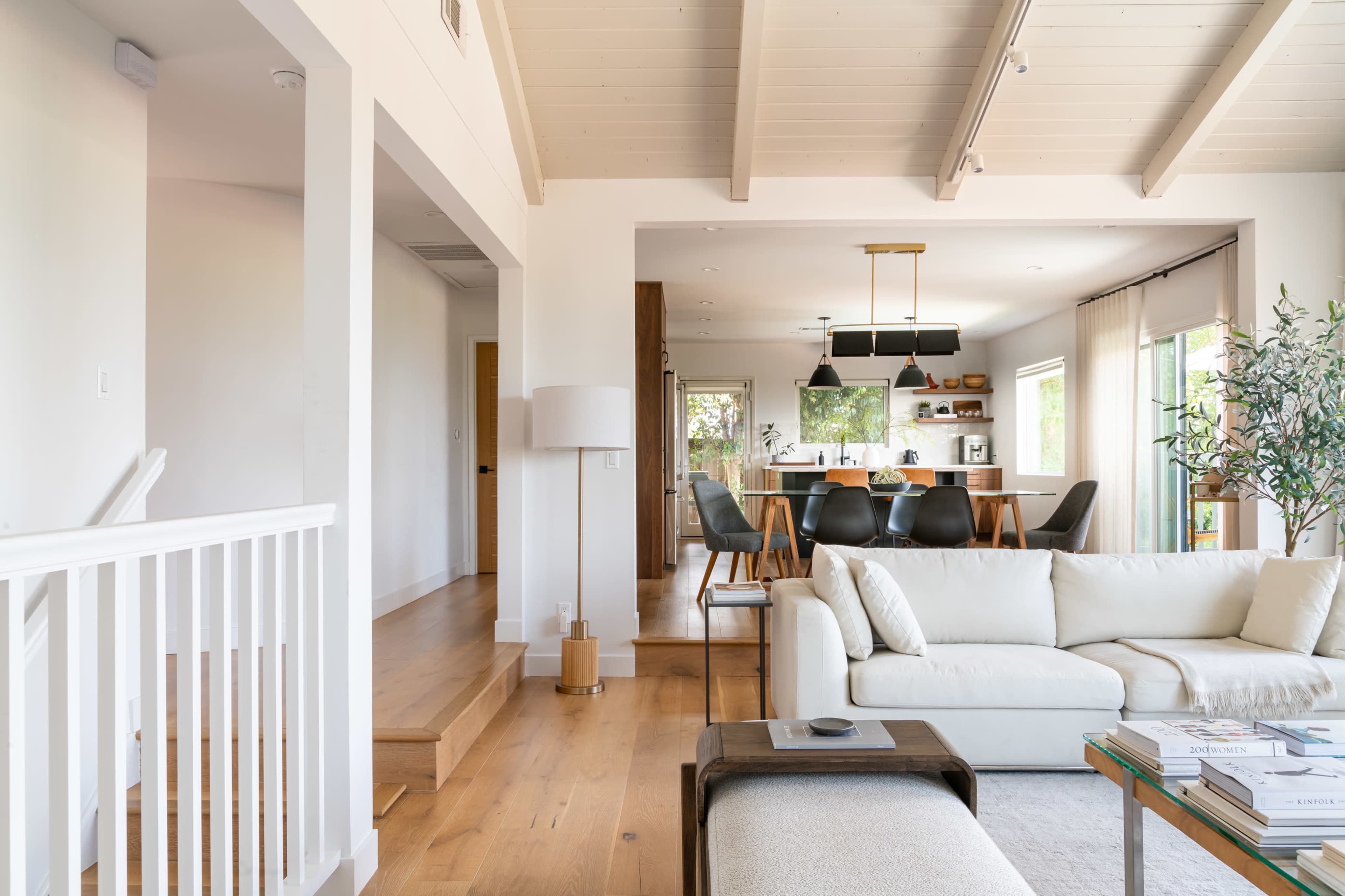 A modern, open-concept living area with a sofa in the foreground, a dining table in the background, and steps leading to another room.