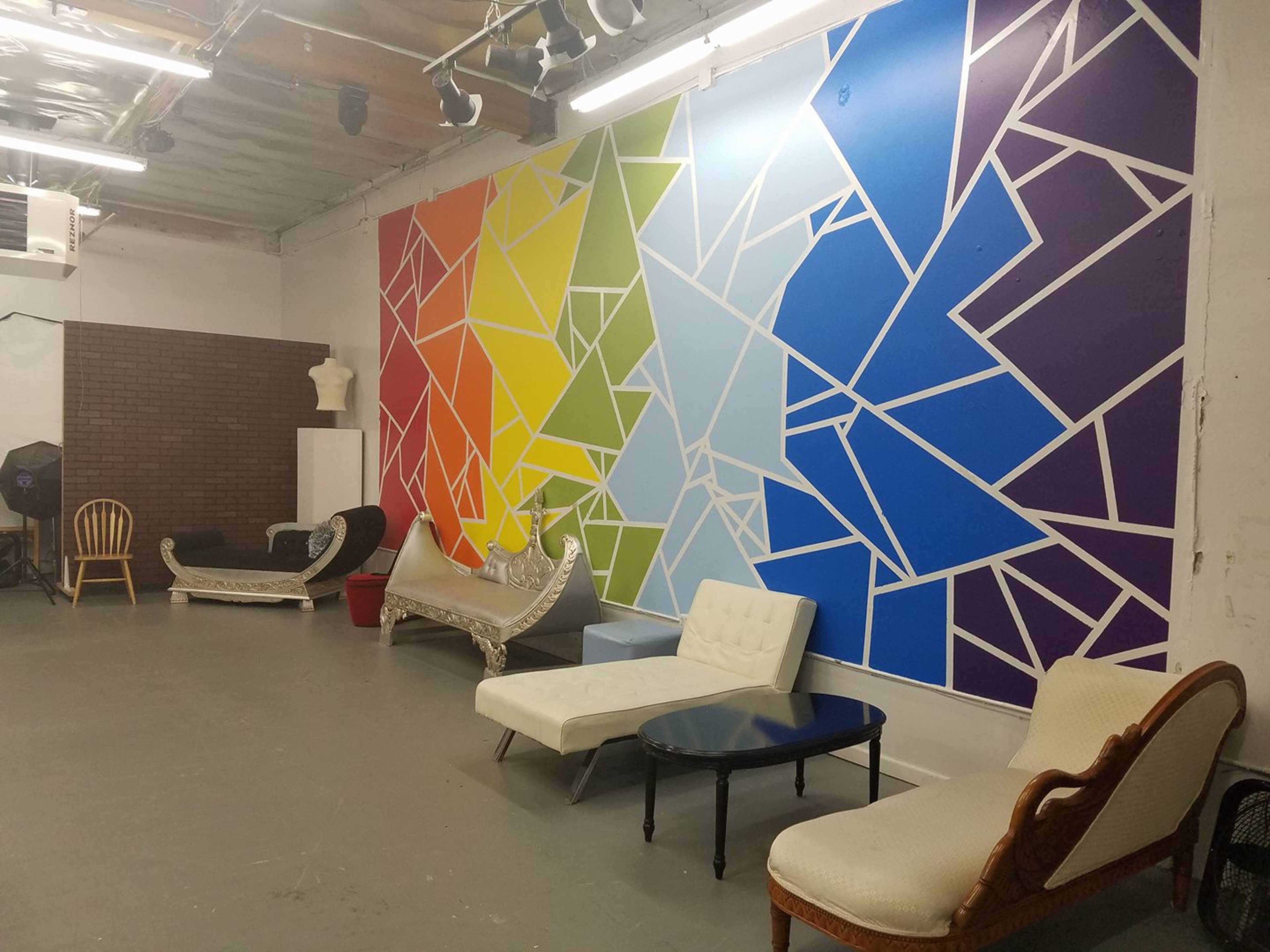 The image shows a spacious room with a colorful geometric mural on one wall and various couches arranged along the floor.