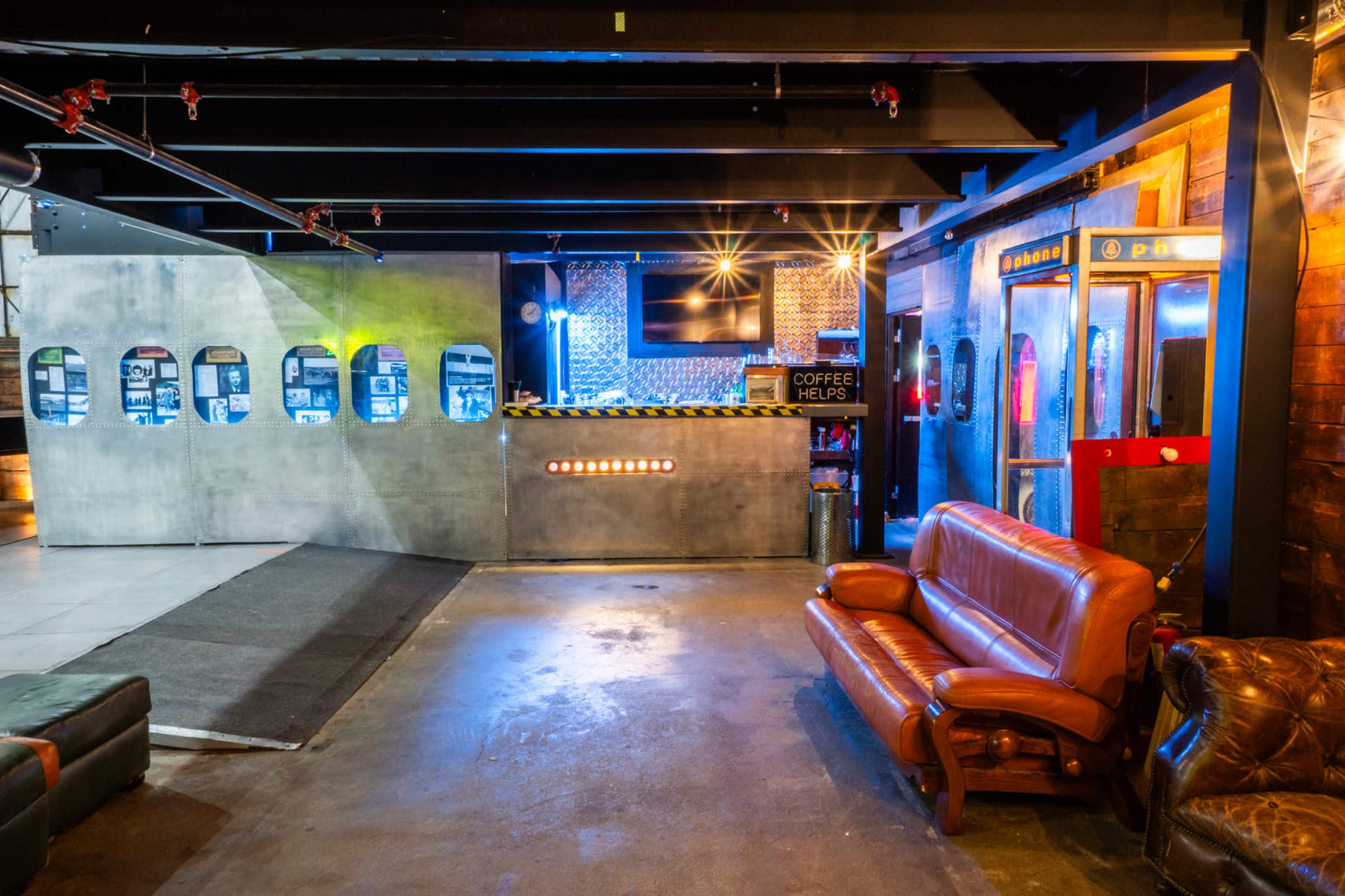 The image shows an industrial-style interior with a bar area and a seating area that includes a brown leather sofa.