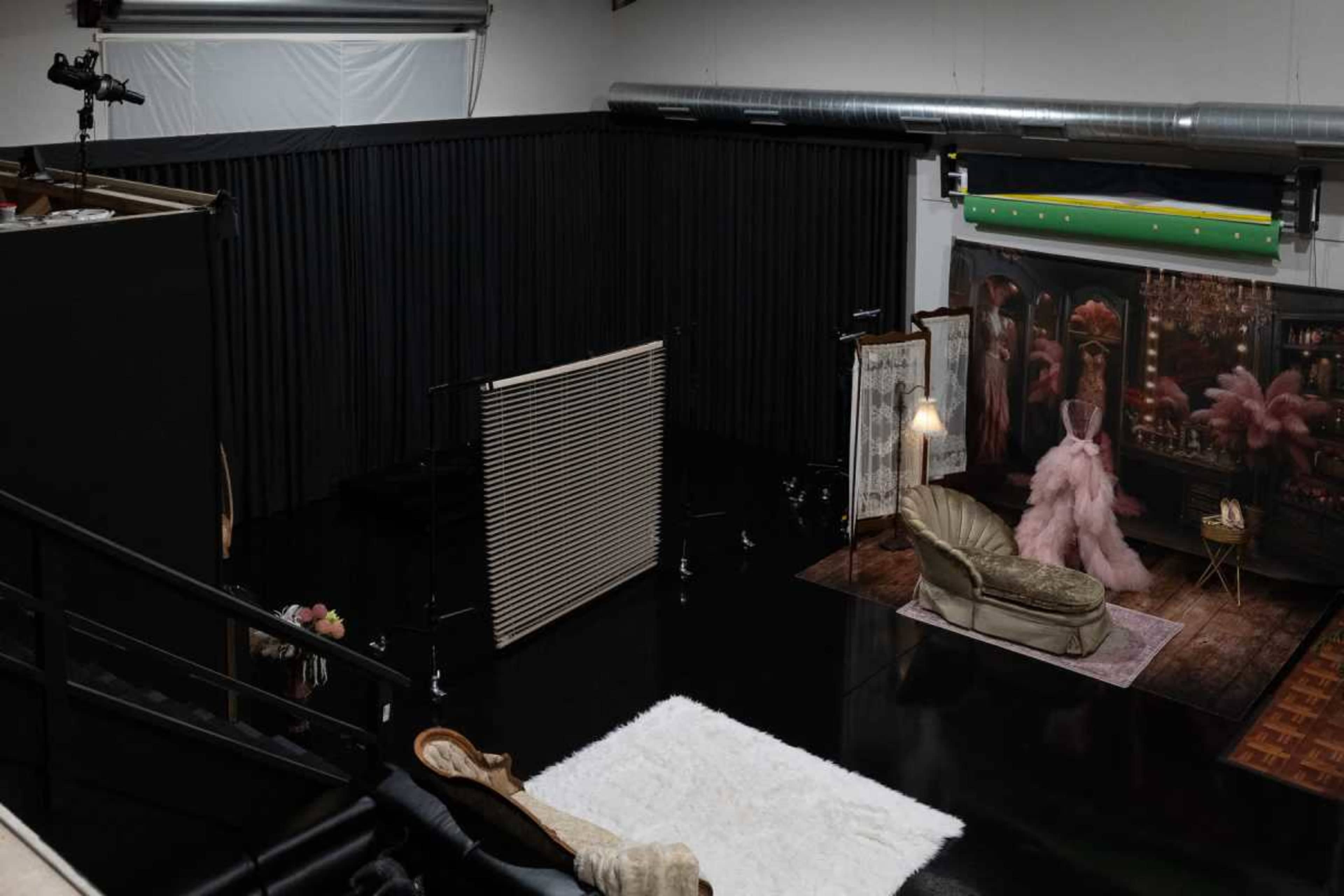 The image shows a spacious photo studio featuring a black floor, a white rug, a plush couch, and various backdrops and lighting equipment.