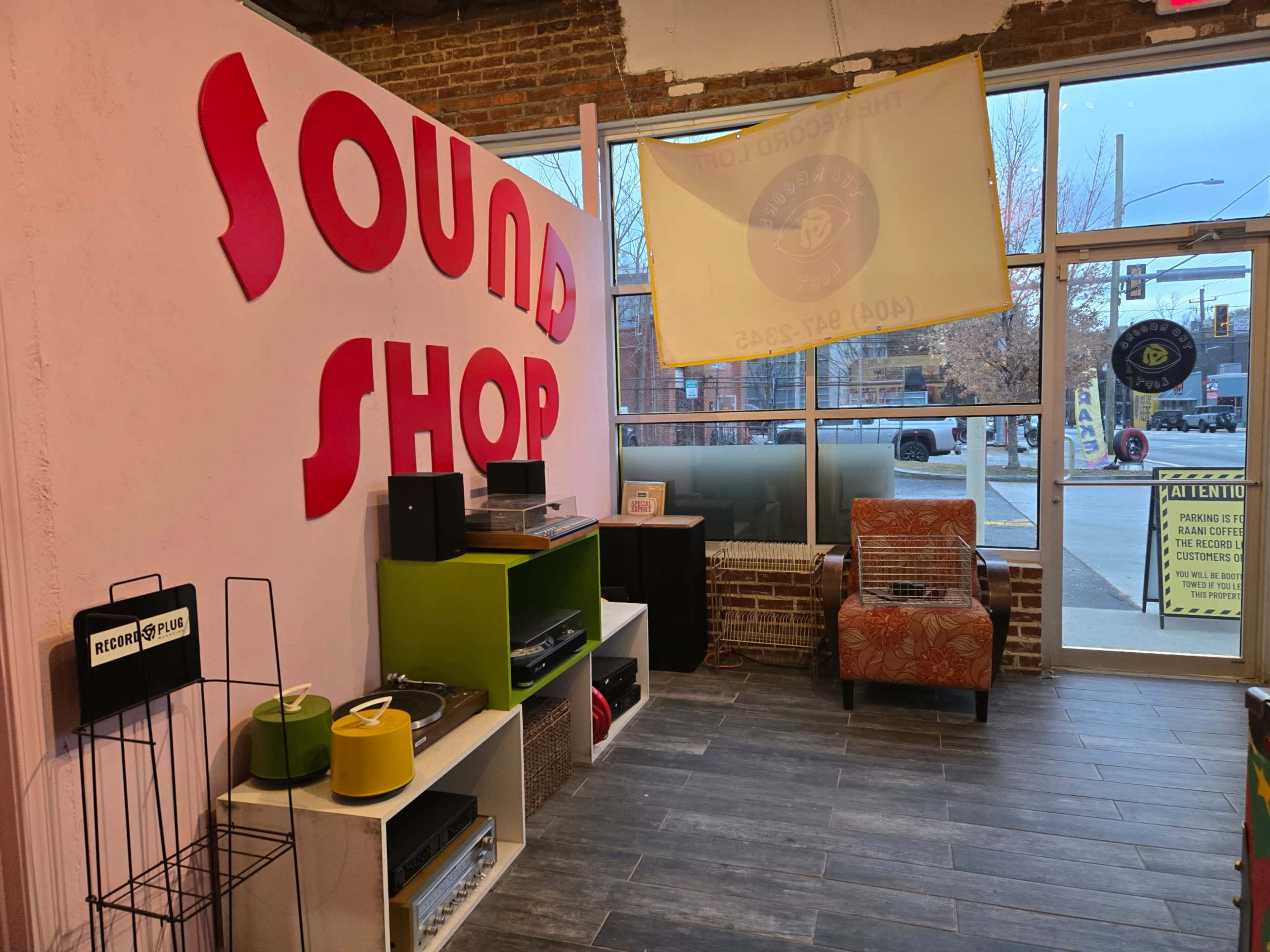 The interior of a store called "Sound Shop" features colorful shelving with audio equipment and an orange armchair, illuminated by natural light from the front windows.