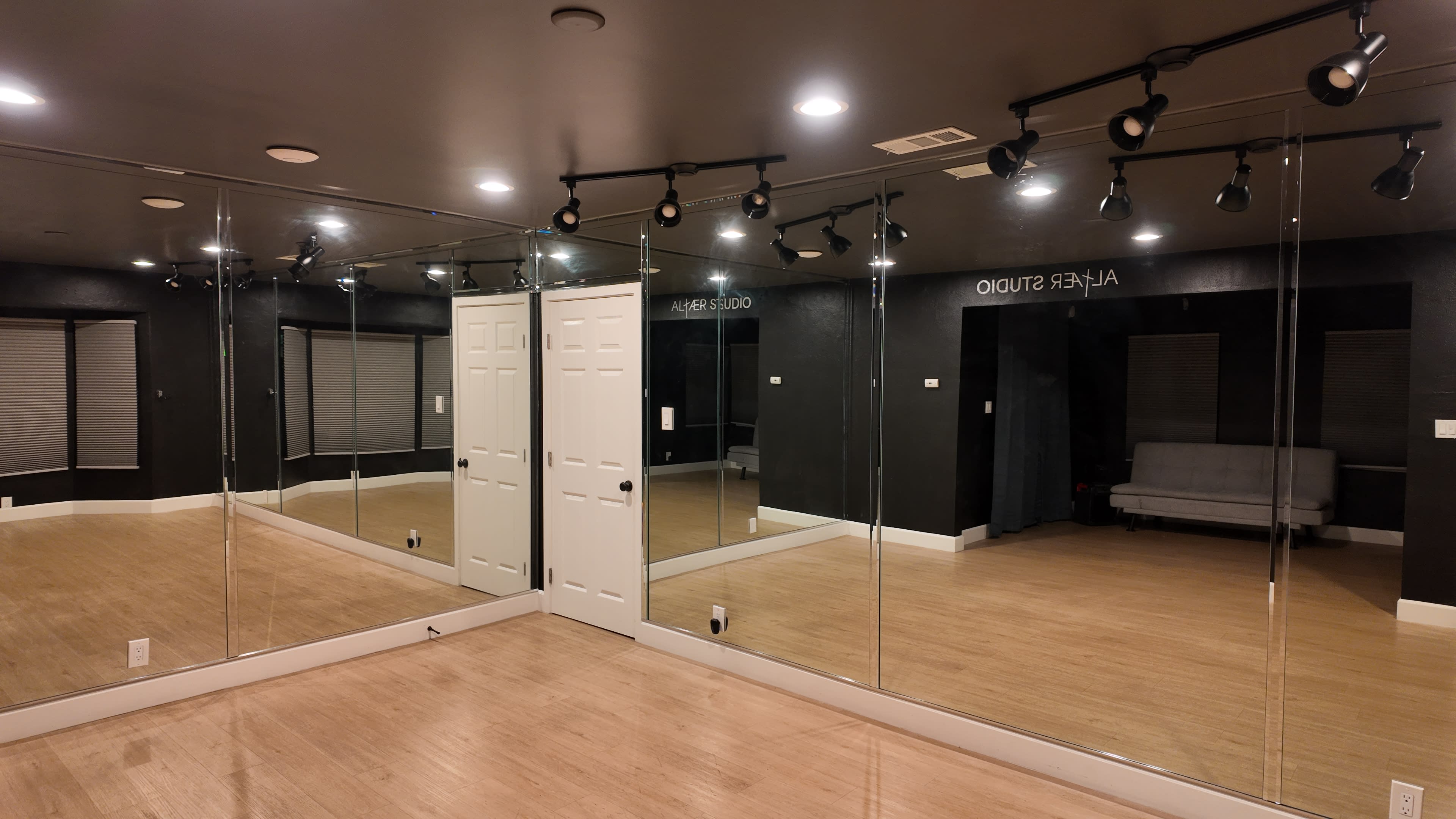 The image shows a room with mirrored walls, multiple ceiling lights, and a folding door leading to another space that includes a sofa.