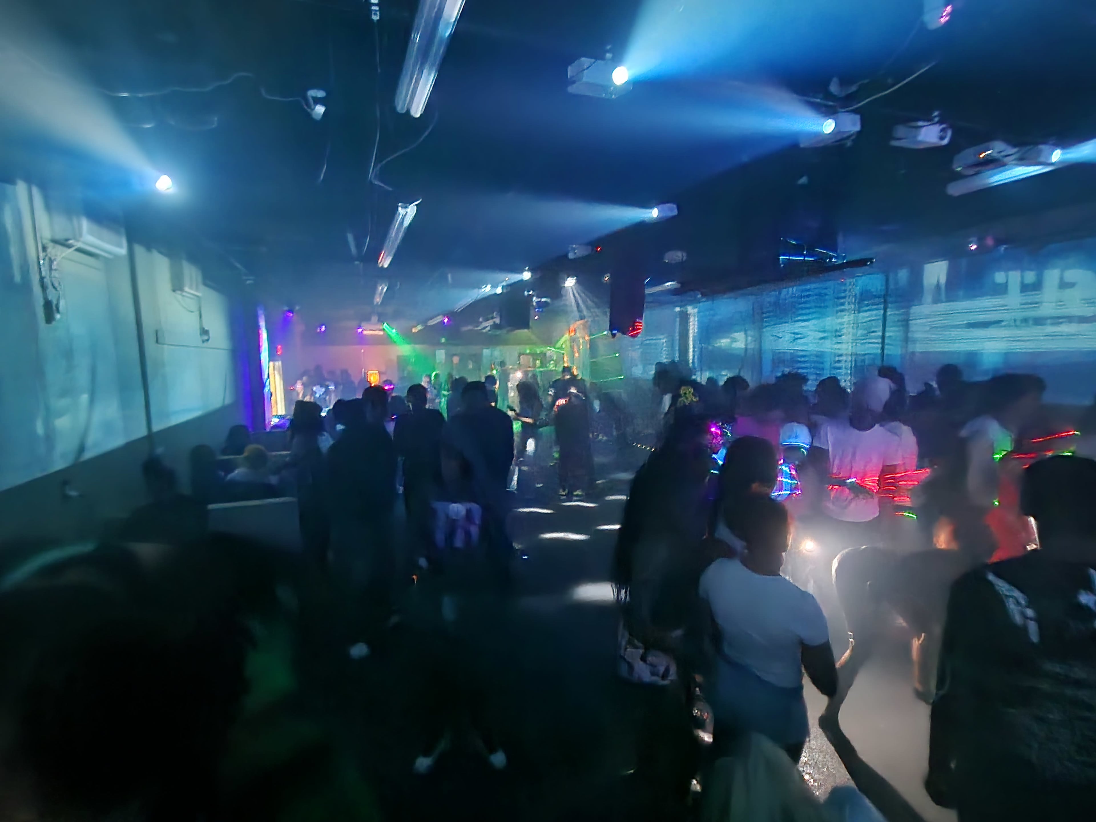 A crowded nightclub is filled with people dancing under colorful lights and fog.