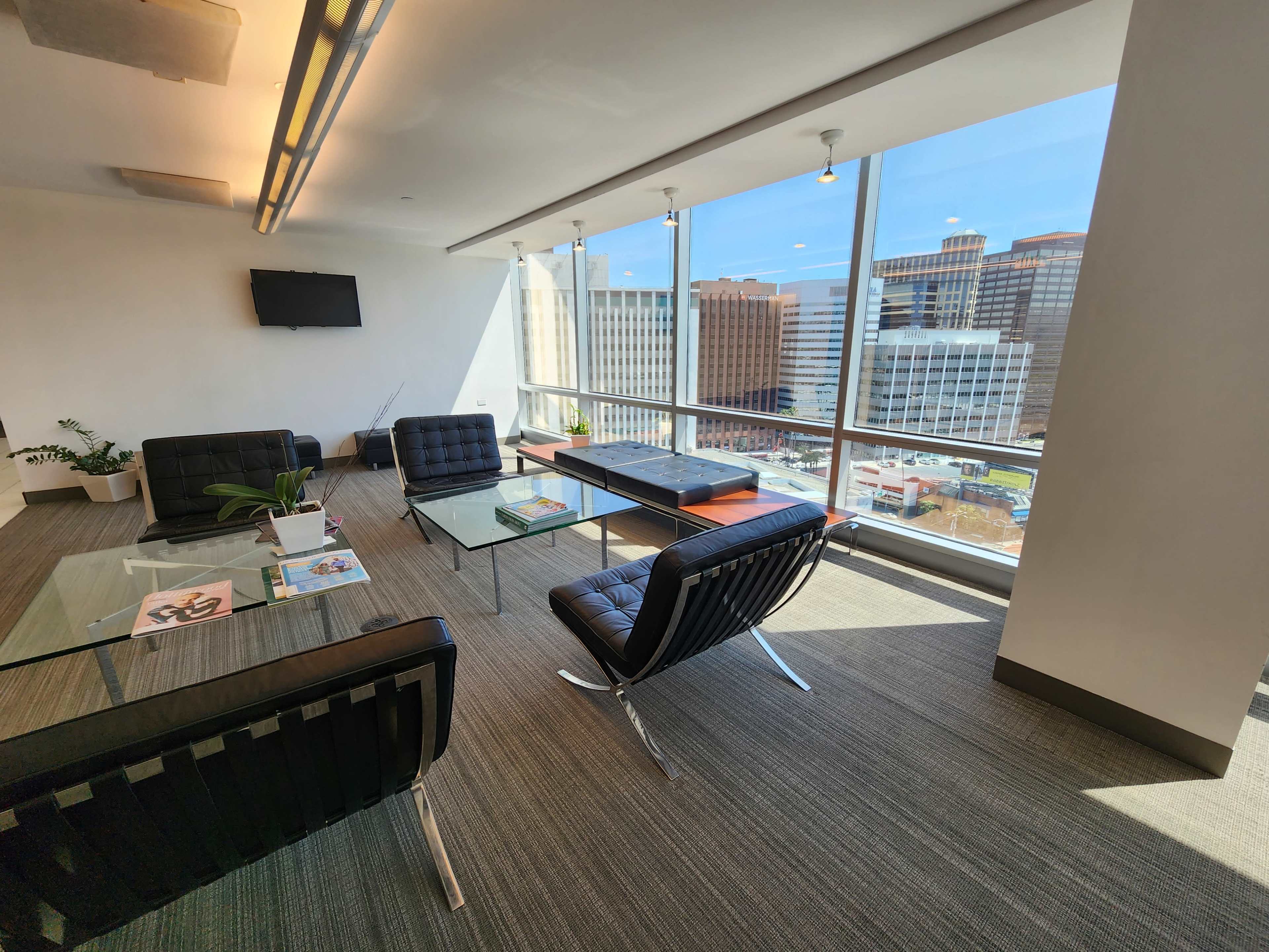 A brightly lit modern office lounge with black chairs, glass tables, and large windows overlooking a cityscape.
