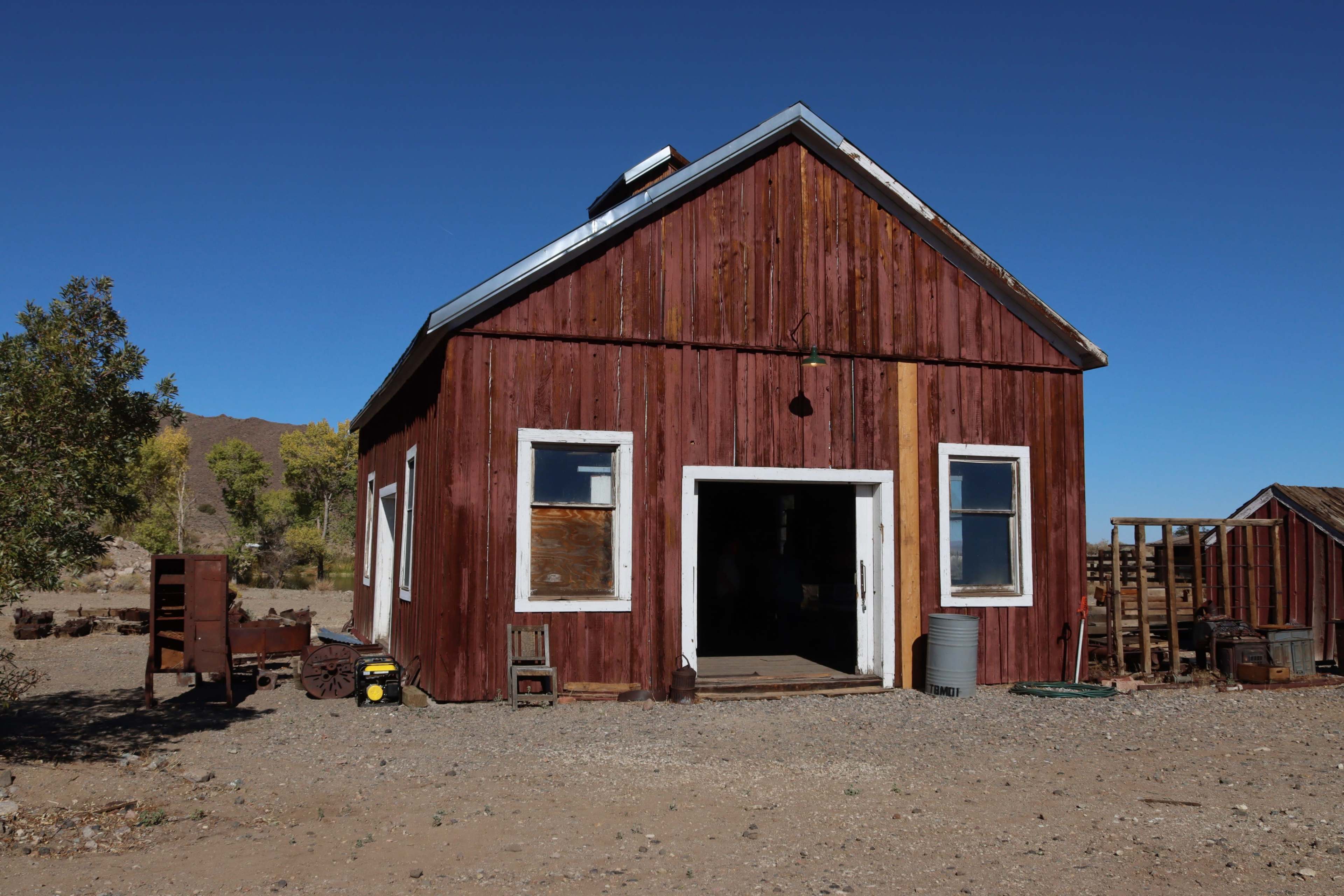 A rustic wooden building with a red exterior and white trim stands in an arid landscape under a clear blue sky.