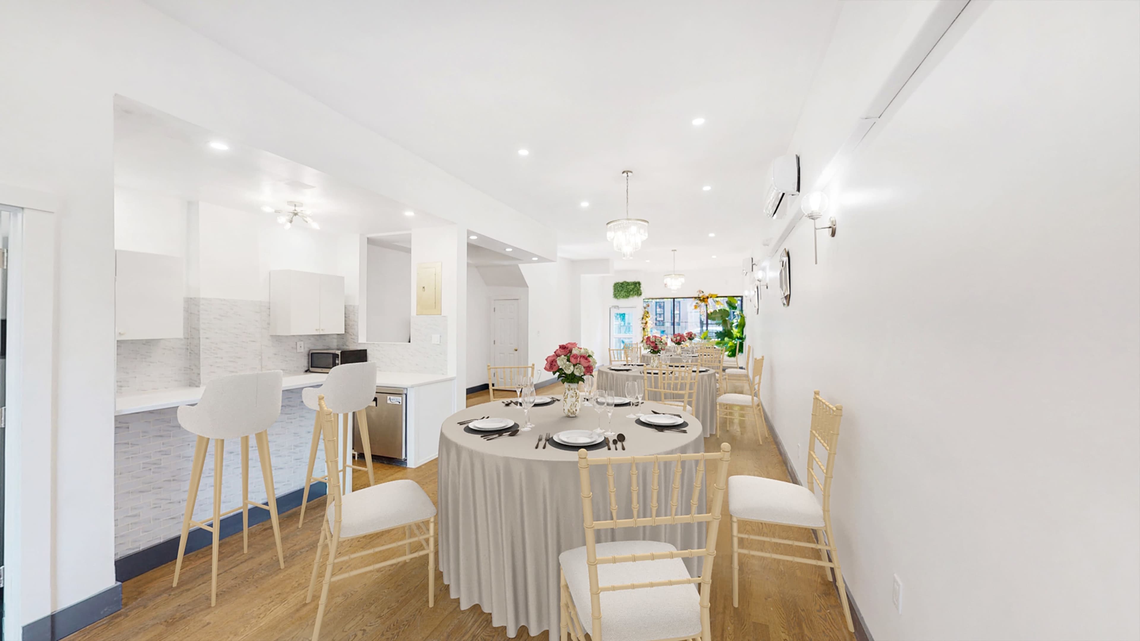 A dining area set with a round table and chairs, featuring floral centerpieces and a modern kitchen in the background.