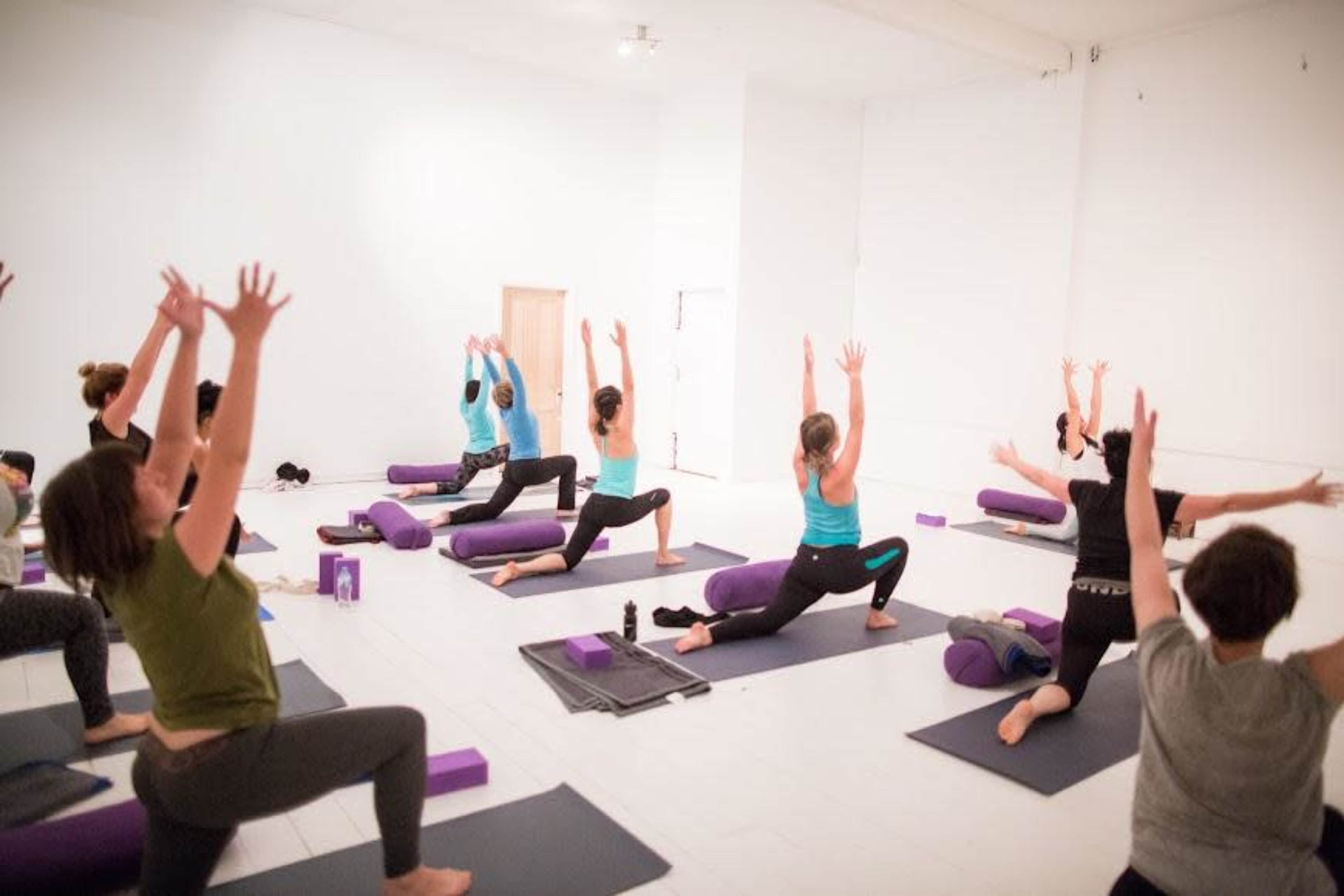 A group of people practices yoga in a spacious, bright studio with mats and props.