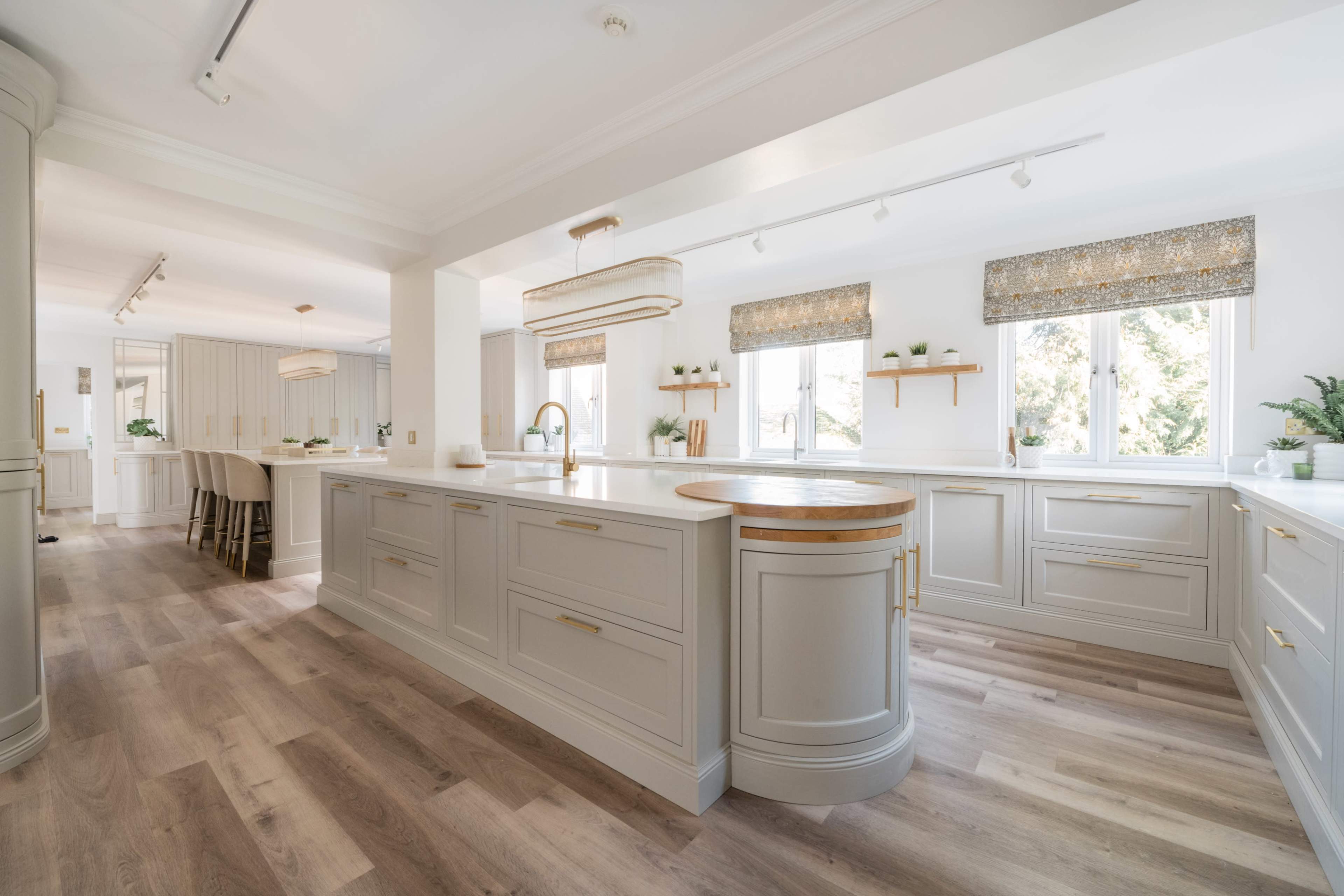 A modern kitchen with light gray cabinetry, an island with a wooden accent, and large windows allowing natural light to enter the space.