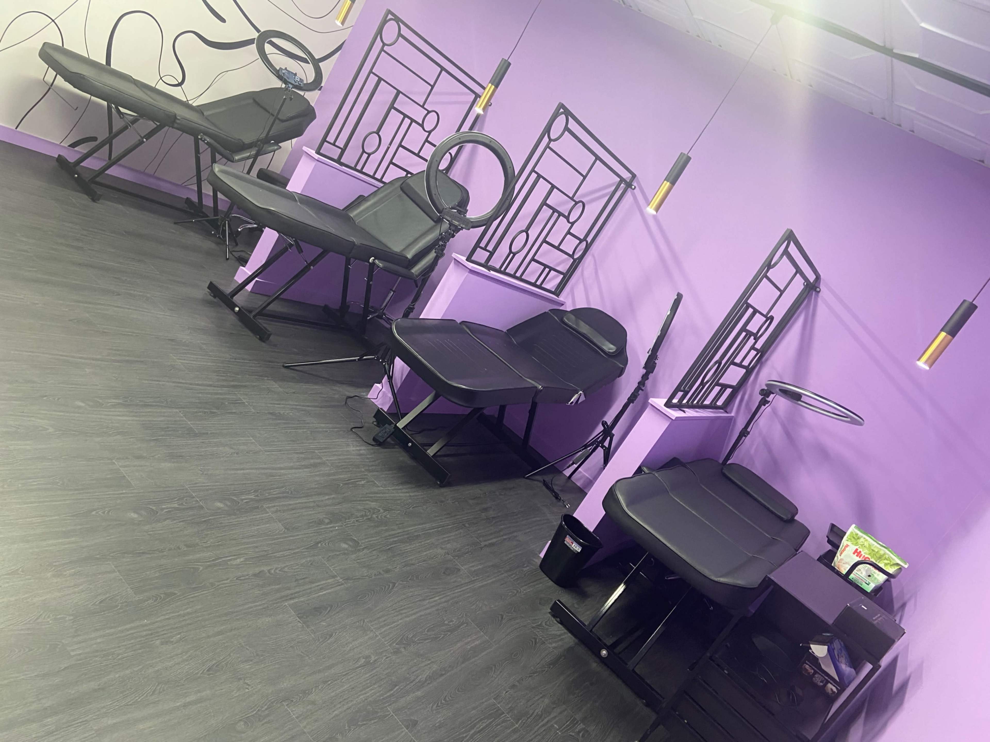 The image shows a modern, minimalist room with several black treatment tables and purple walls, featuring decorative wall art.