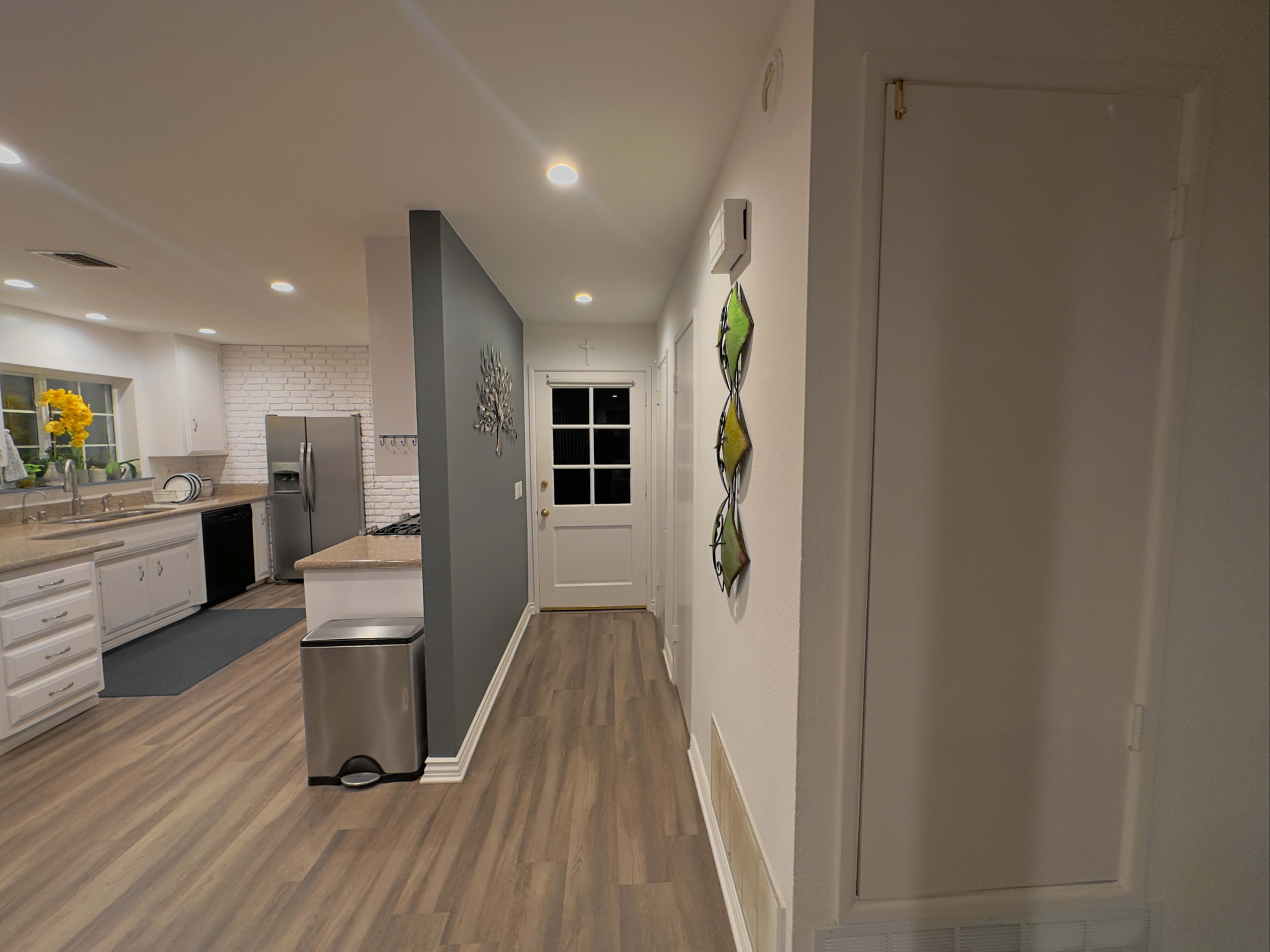 A modern kitchen area leading to a hallway with a door at the end and a small storage closet on the right.