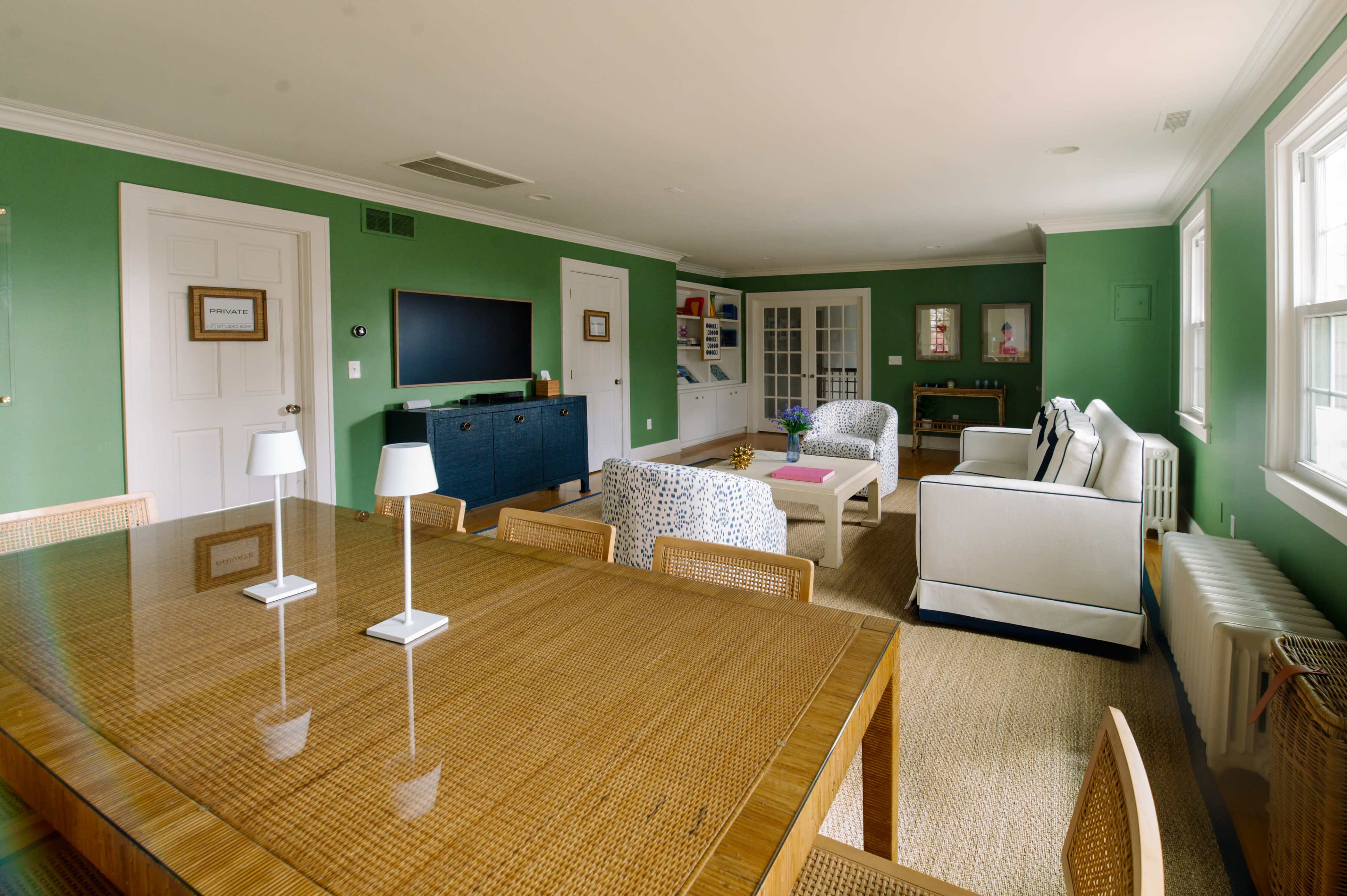 The image shows a spacious living room with green walls, a large dining table, and comfortable seating arrangements.