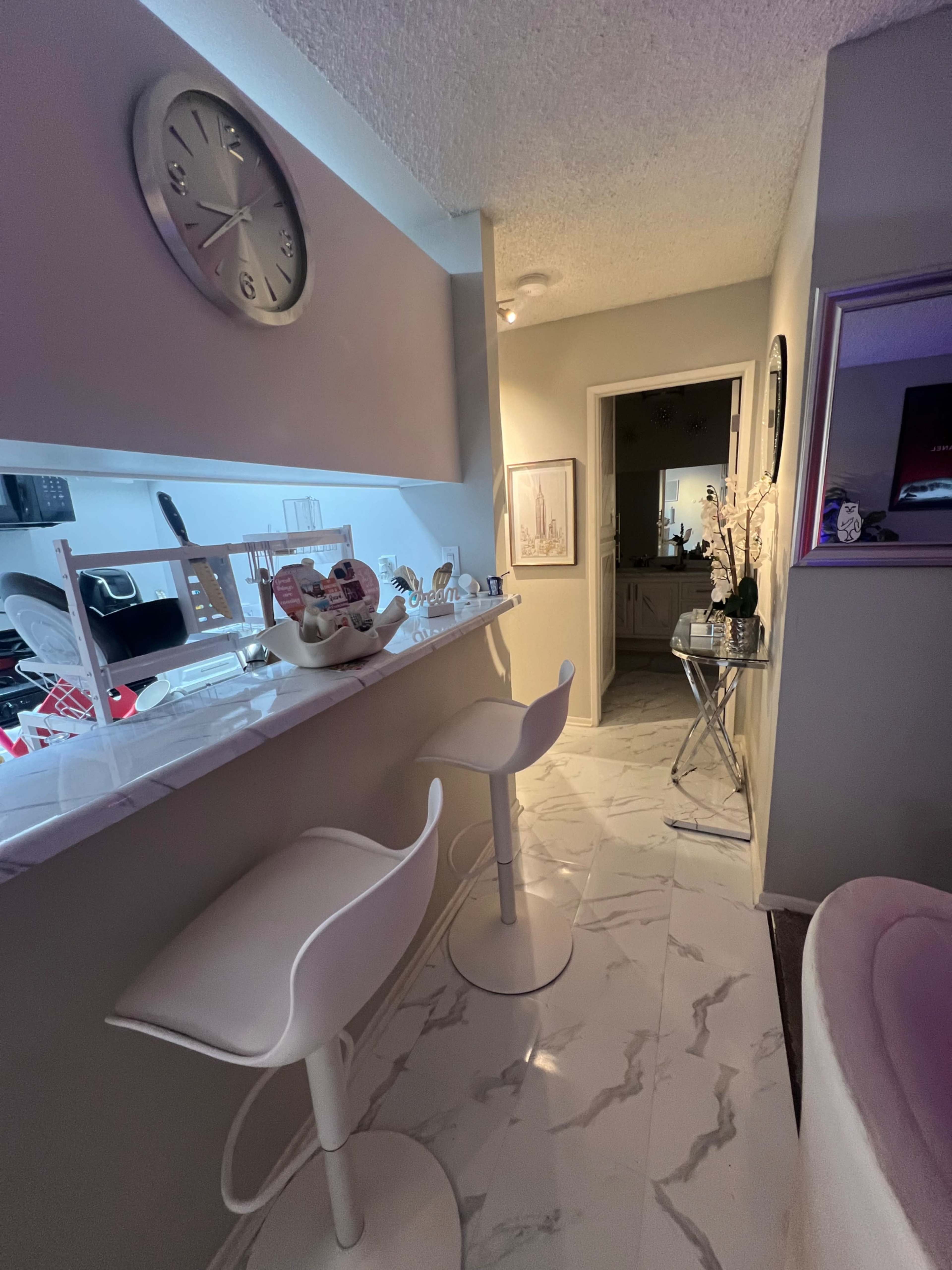 A modern hallway with a bar counter featuring two white stools, leading to a bathroom door at the end.