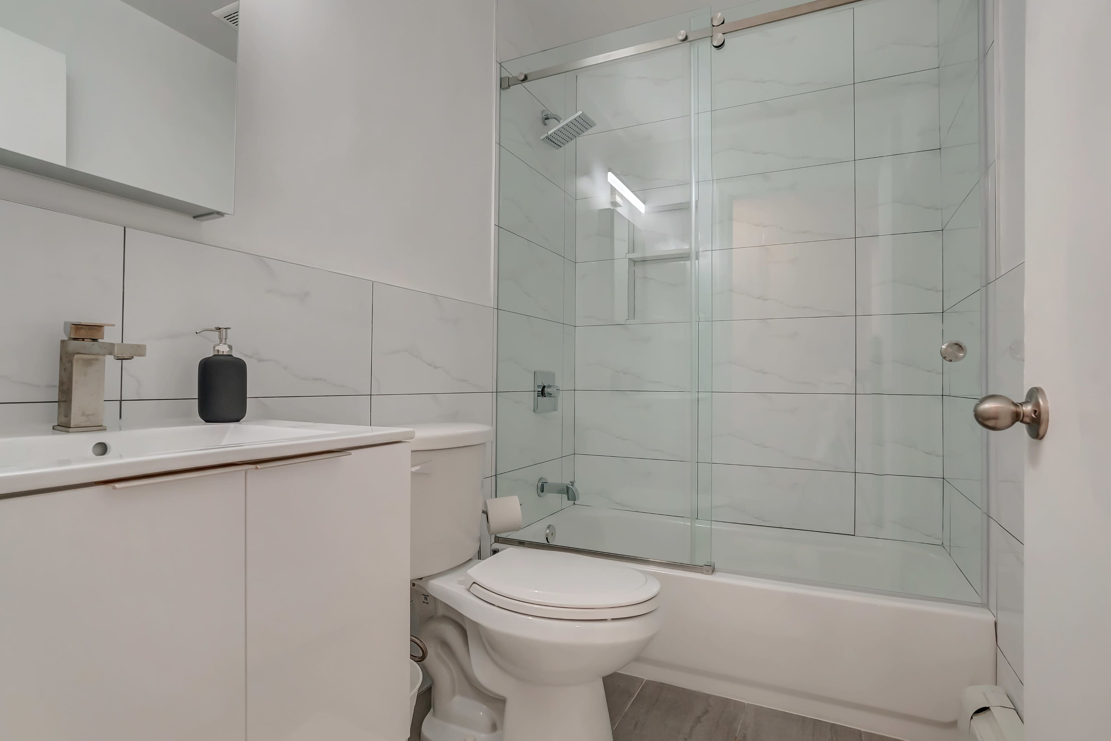 A modern bathroom featuring a bathtub with a glass shower enclosure, a white toilet, and a sink with a mirror above it.
