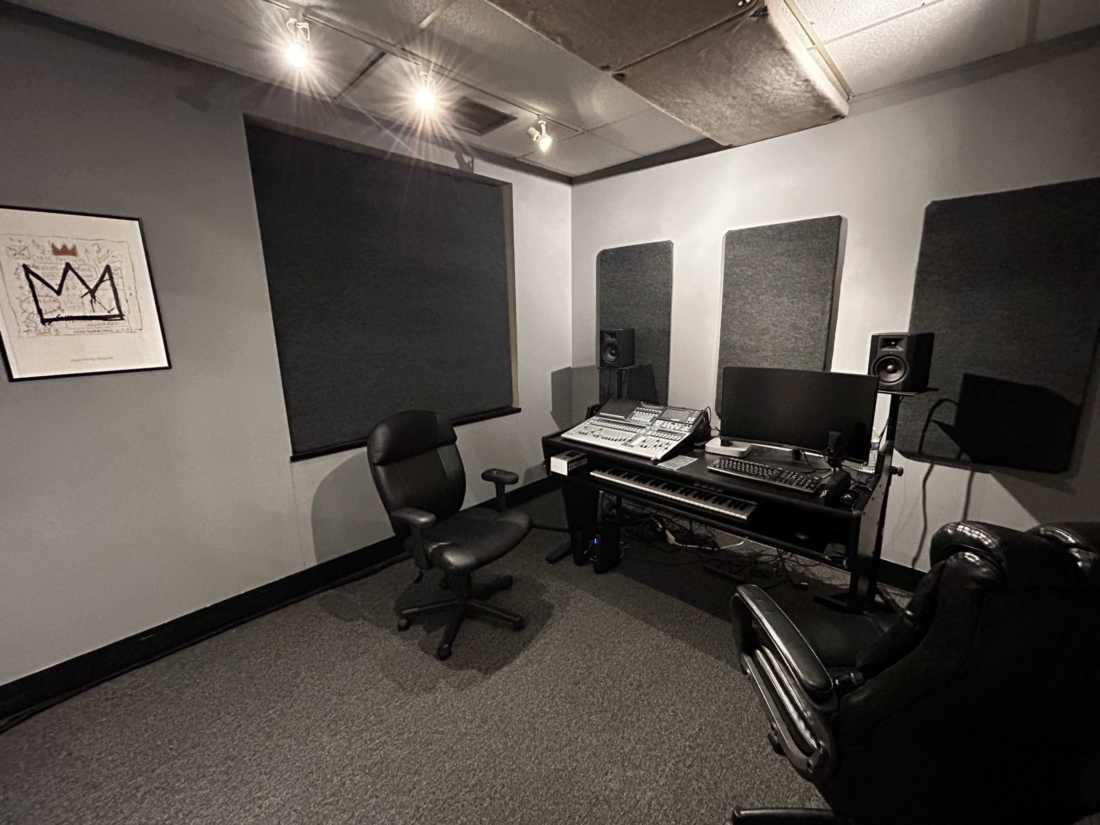The image shows a music production studio with a desk, computer equipment, and soundproofing panels on the walls.