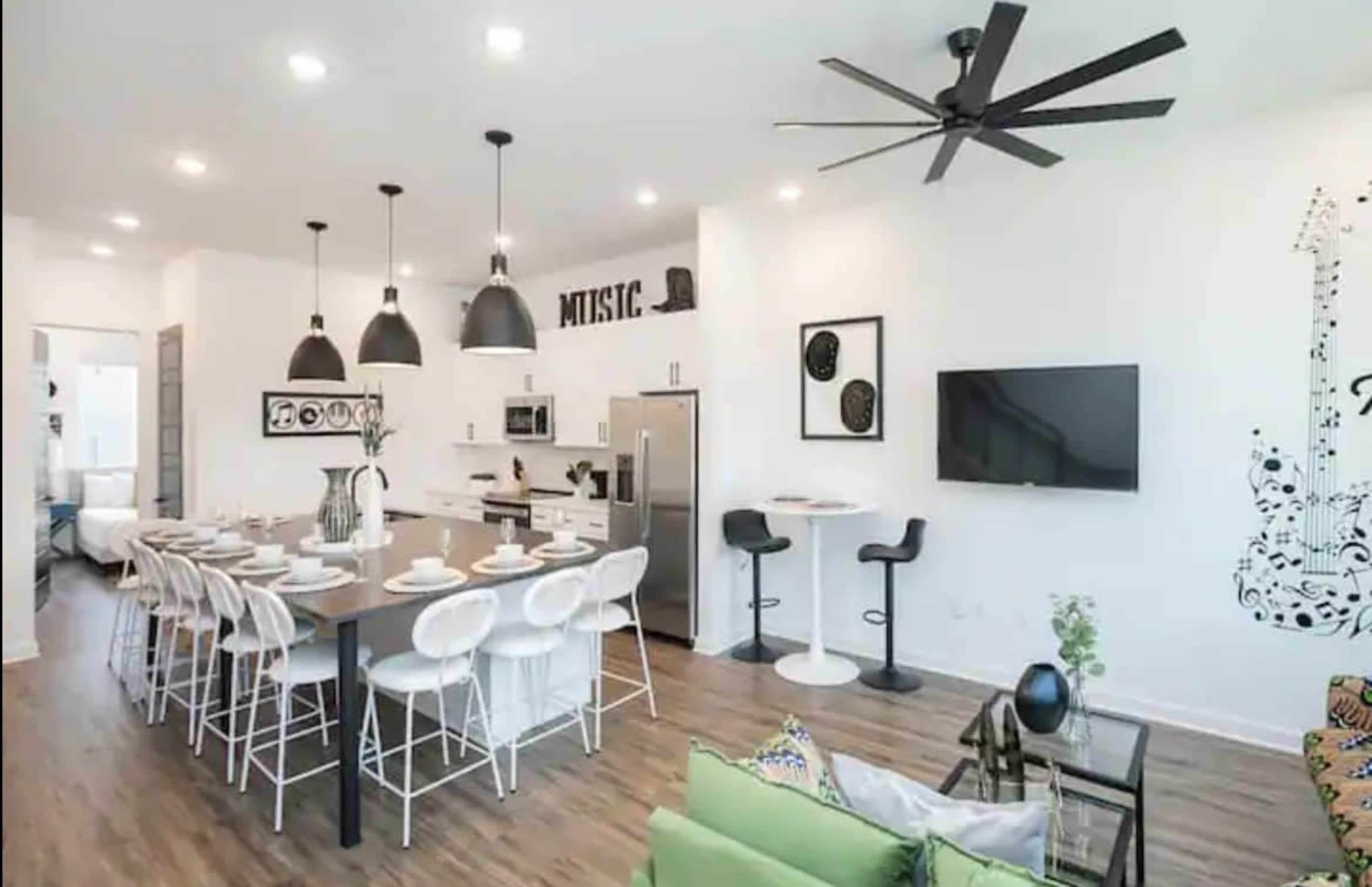 A modern kitchen and dining area features a large table with white chairs, pendant lighting, and decorative music-themed elements on the walls.