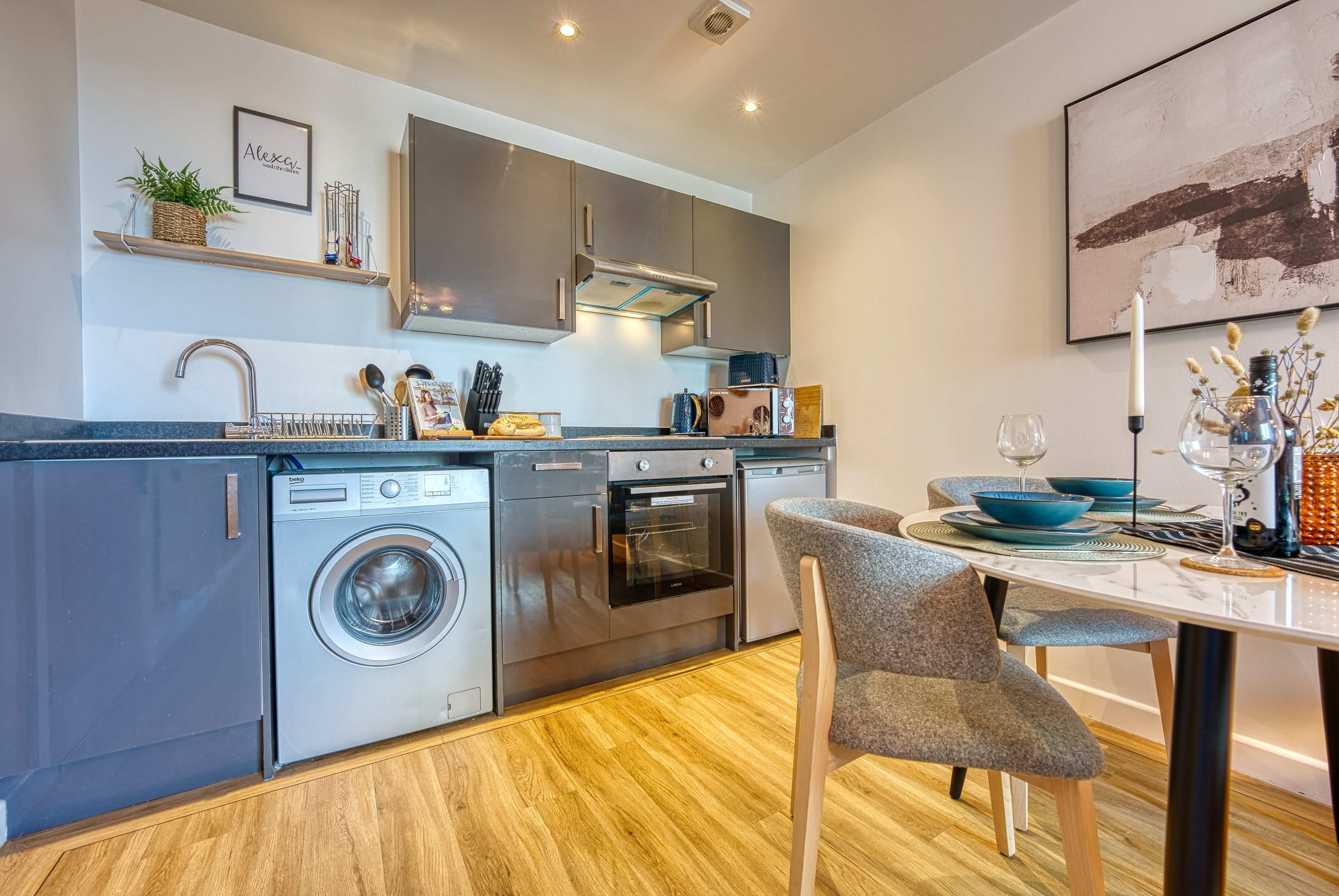 A modern kitchen with stainless steel appliances, a washing machine, and a dining table set for two.