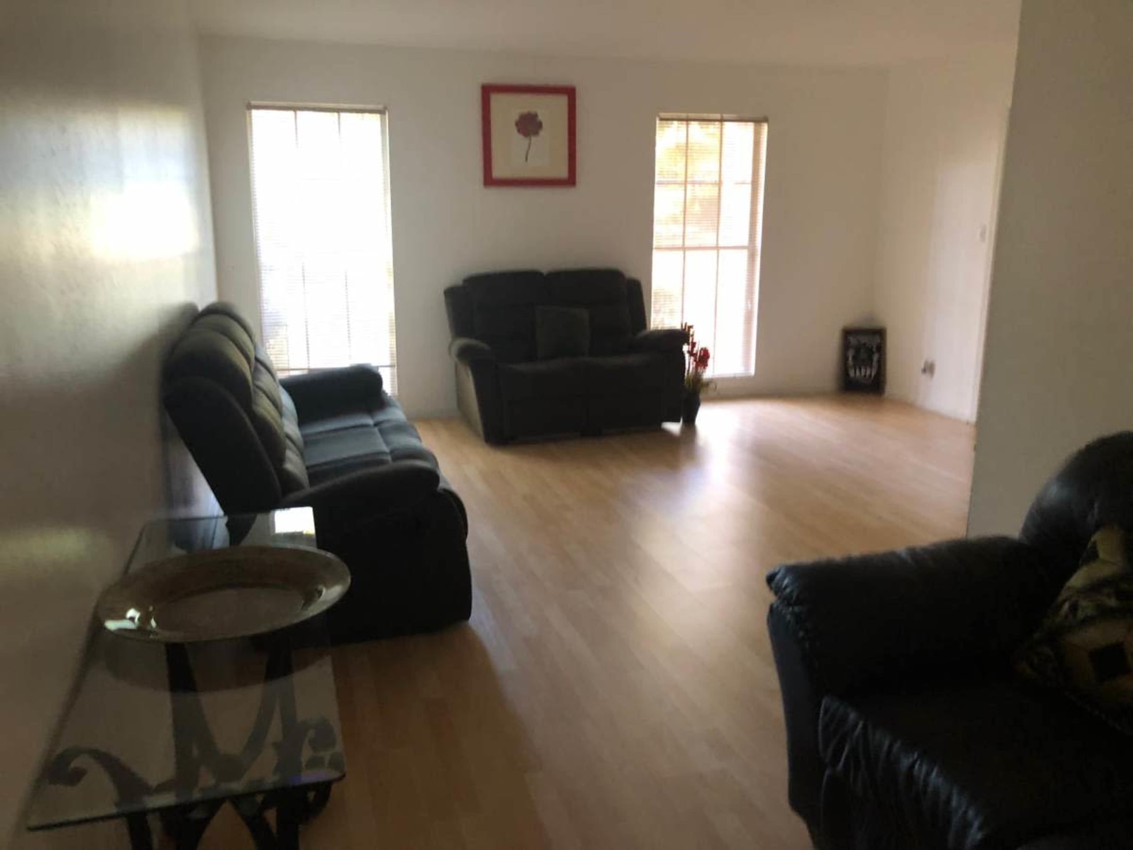 A bright, empty living room with two sofas, a decorative table, and large windows.