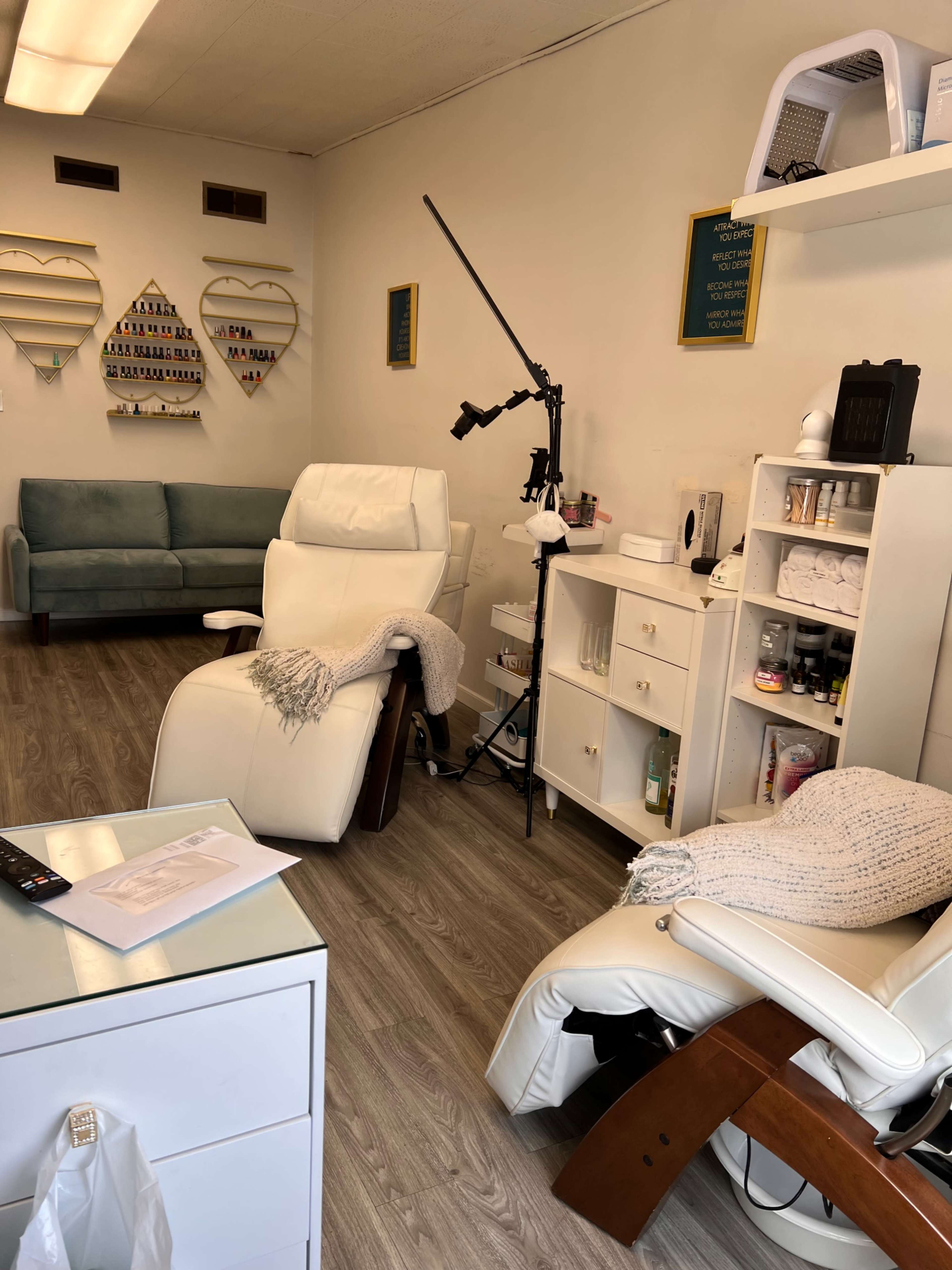 The image shows a nail salon interior featuring two reclining chairs, a manicure station, a couch, and various nail polish displays on the walls.
